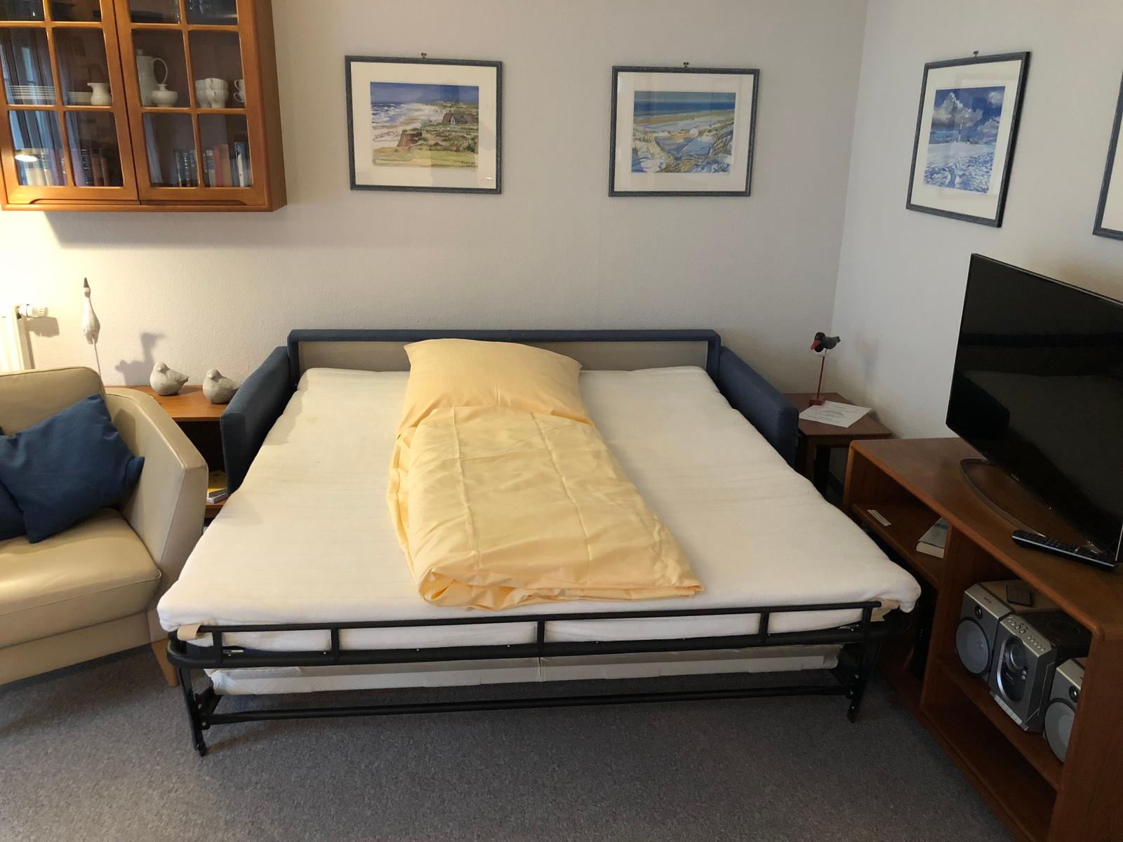 Schlafzimmer mit Bett, Fernseher und Schrank. Wandbilder und Sitzgelegenheit.