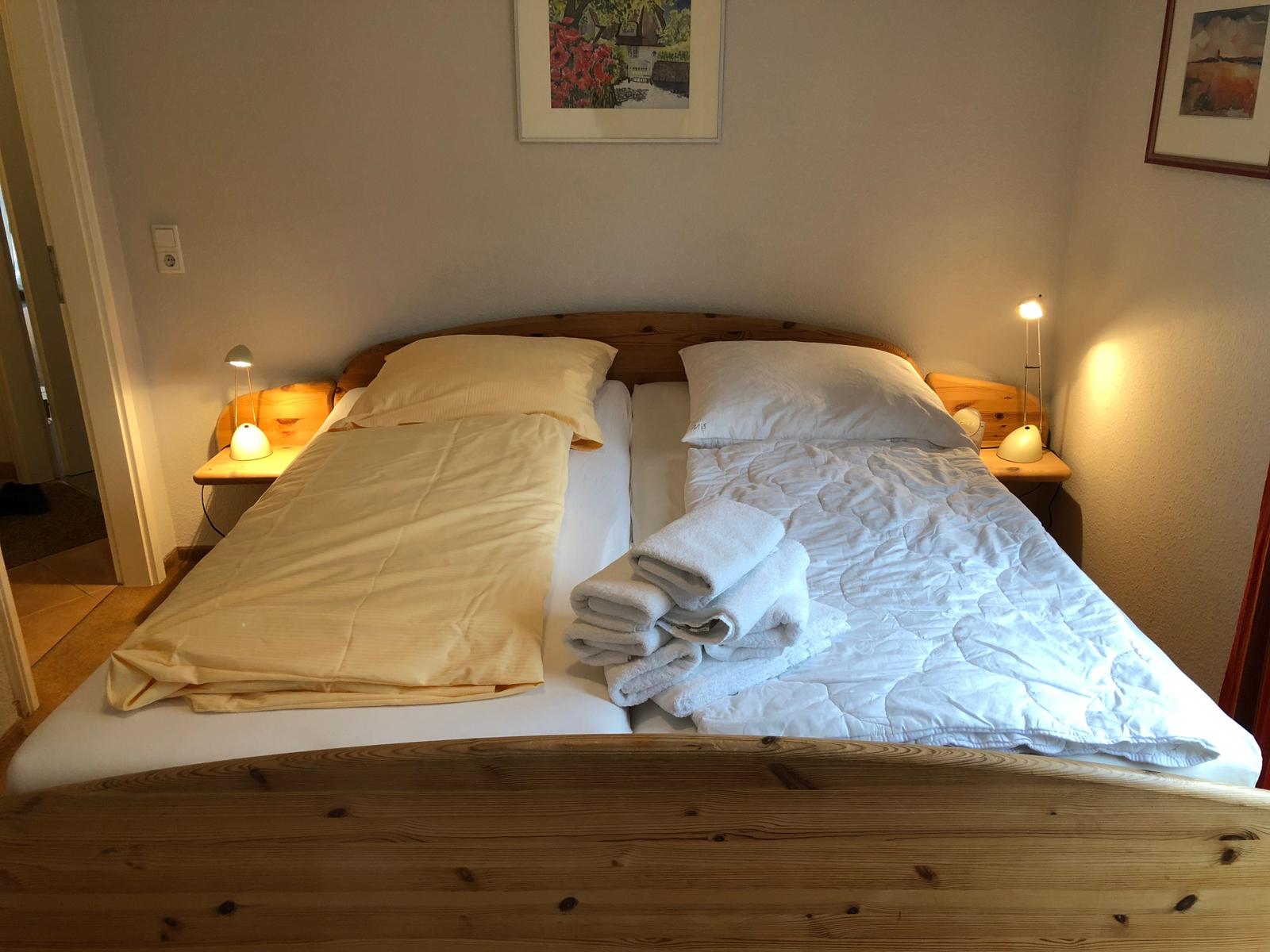 Ein Bett mit Holzgestell, zwei Kissen, Bettwäsche und gefaltete Handtücher.
