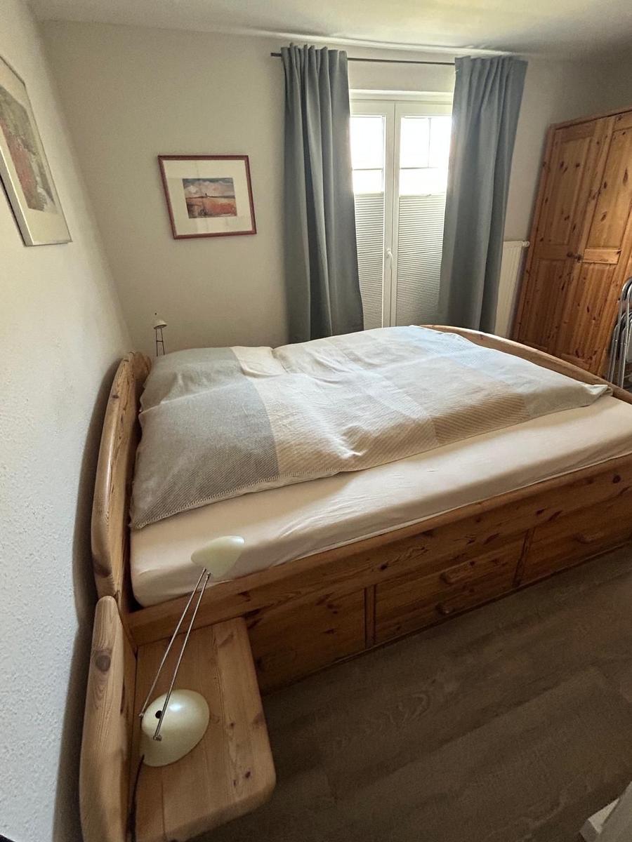 Schlafzimmer mit Holzbett, Vorhängen und Kleiderschrank.