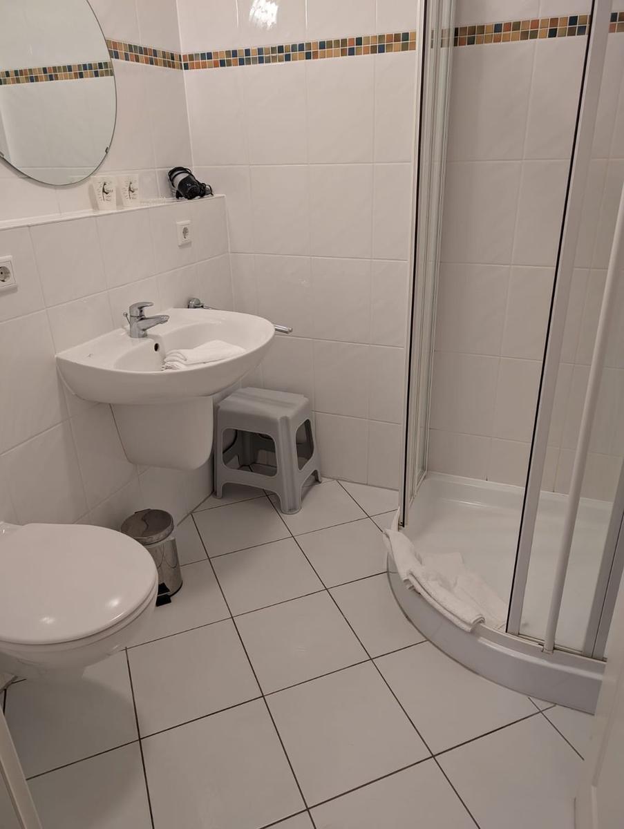 Badezimmer mit Dusche, Waschbecken und Toilette. Fliesenboden und Wandfliesen.