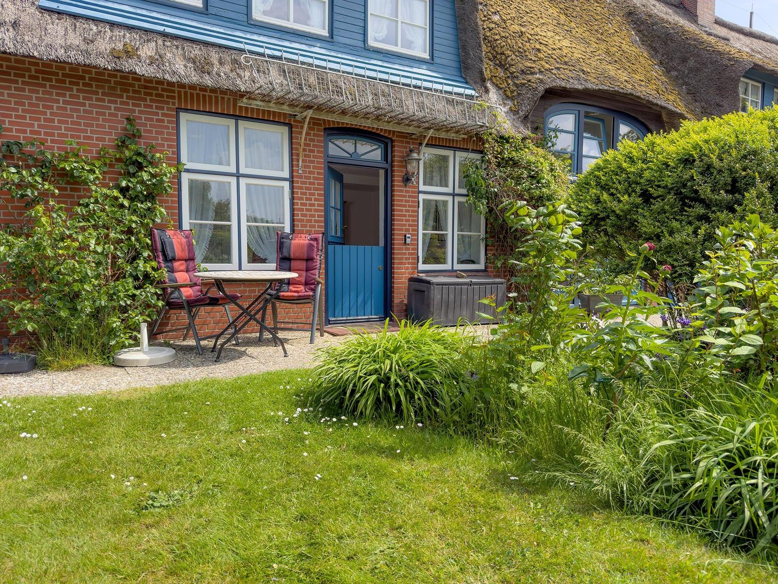 Haus mit strohgedecktem Dach, Garten mit Sitzgelegenheit und grüner Rasenfläche.