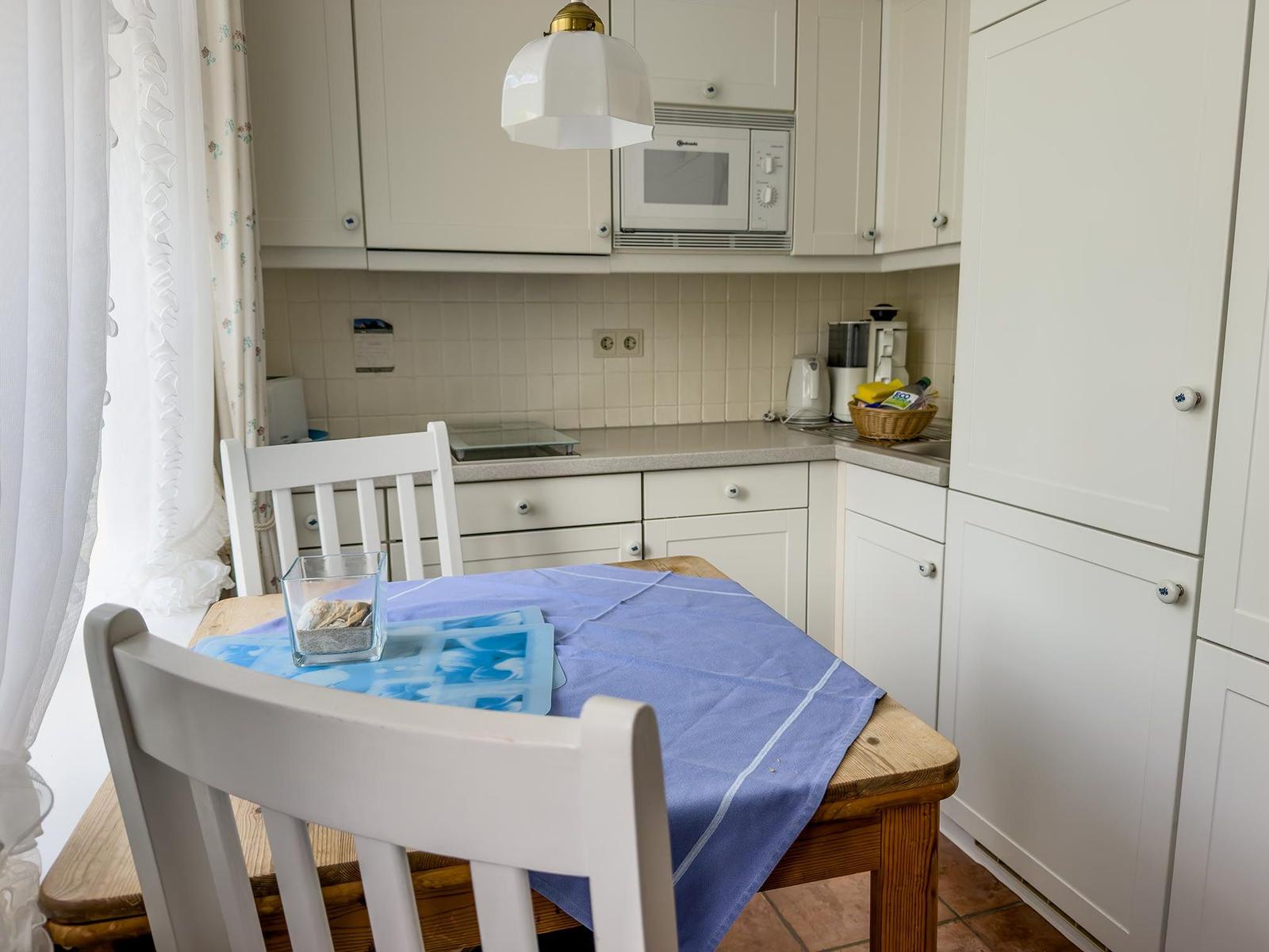 Küche mit Essbereich, weißen Schränken und Holztisch mit blauer Tischdecke.