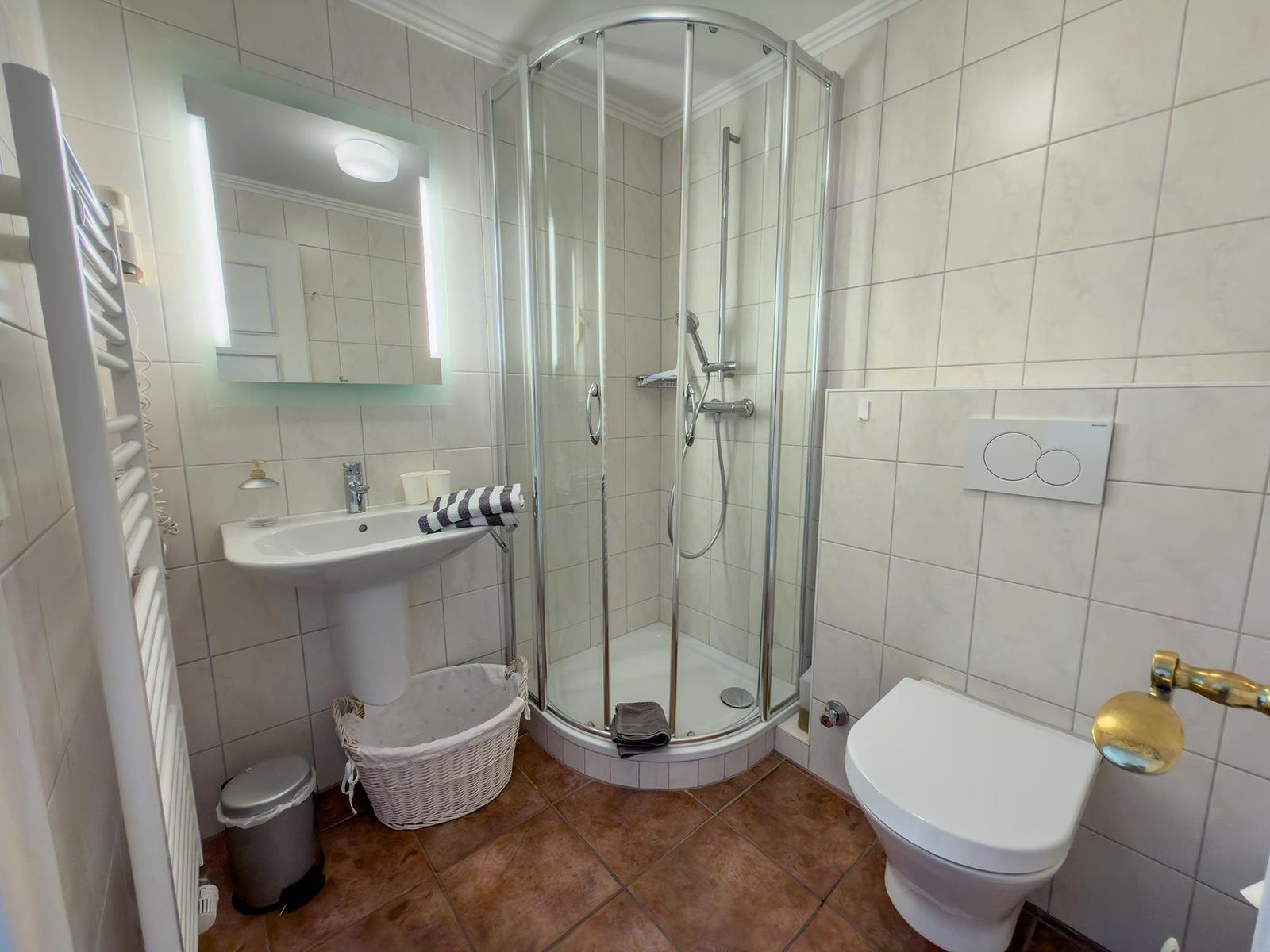 Badezimmer mit Dusche, Waschbecken und WC. Fliesenboden und Spiegelschrank.