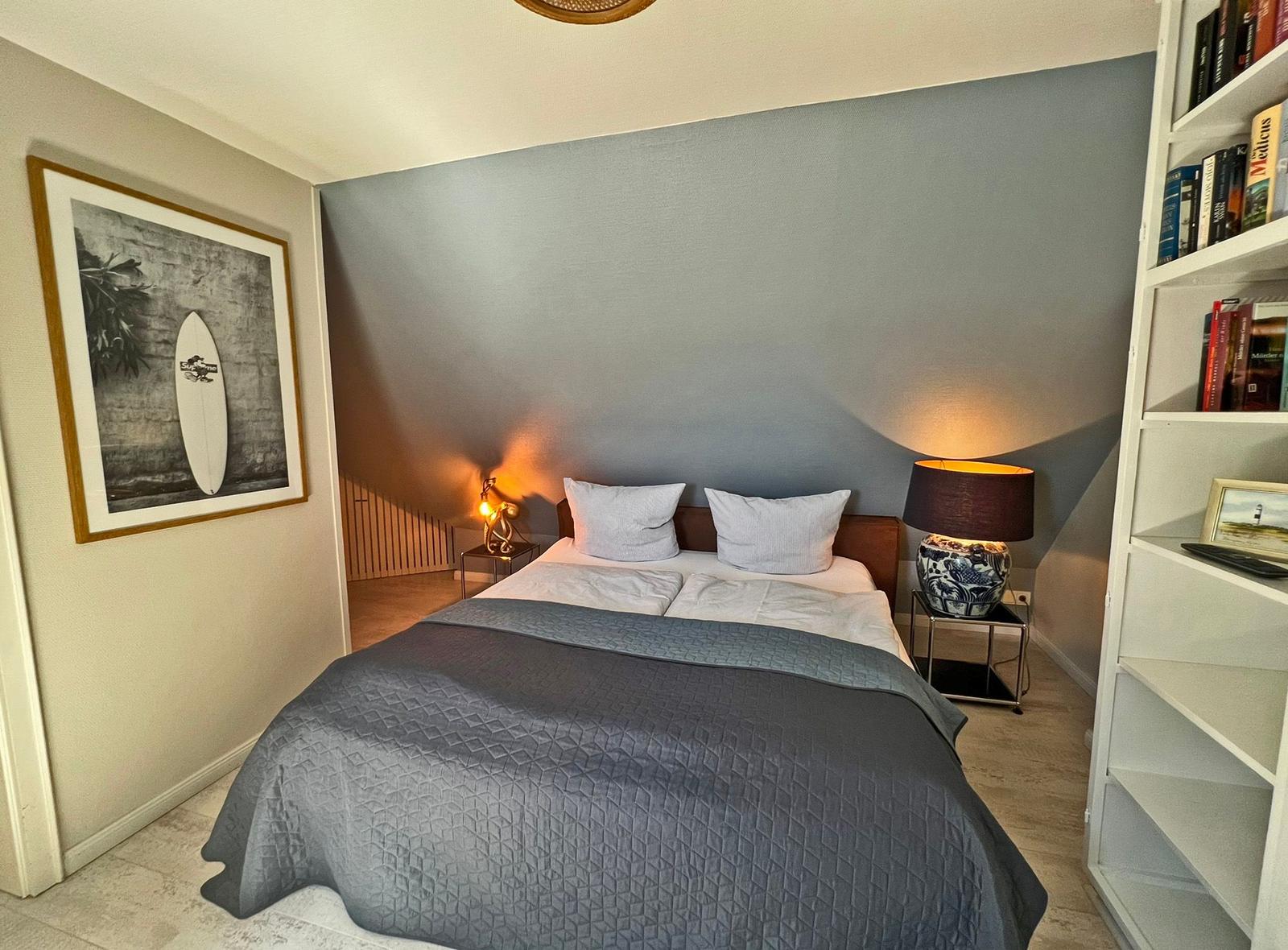 Schlafzimmer mit Bett, Nachttischen und Bücherregal an der Wand.