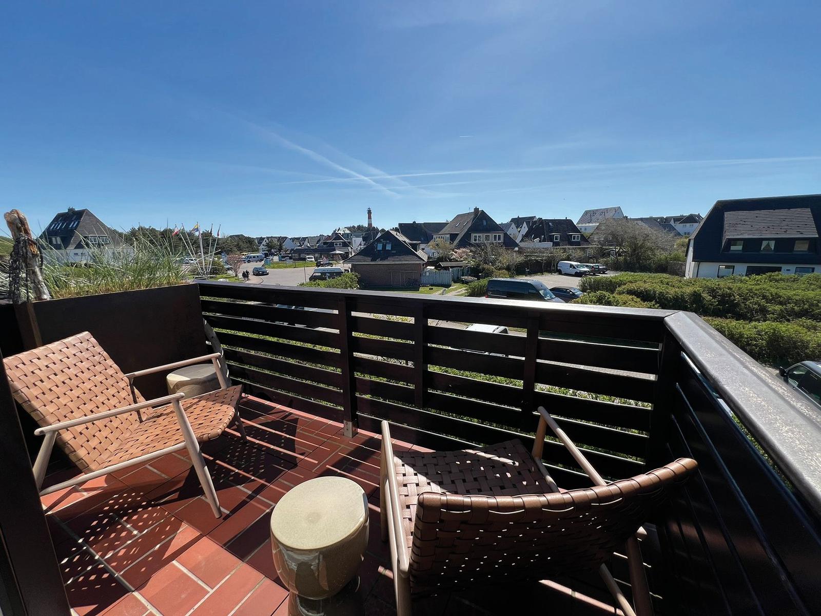 Terrasse mit zwei Stühlen und Tisch, Blick auf Dorf und Leuchtturm.
