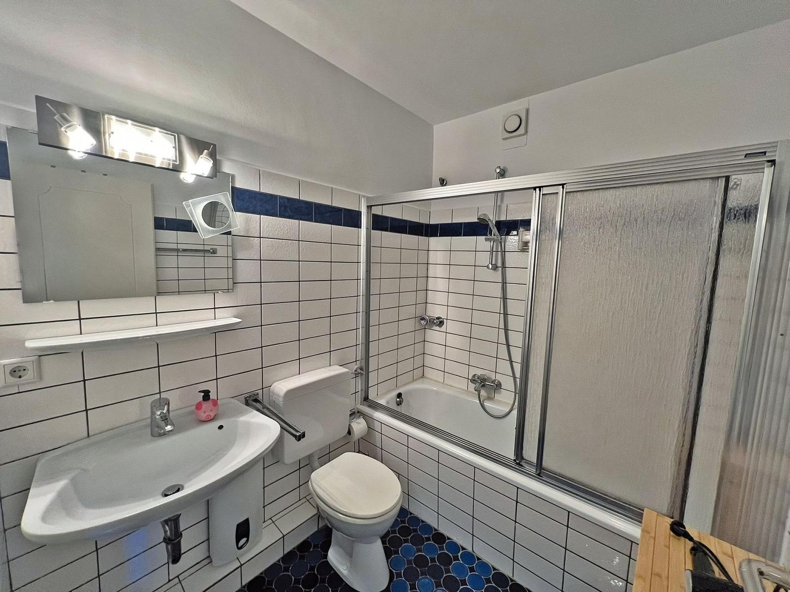 Badezimmer mit Dusche, Toilette und Waschbecken. Fliesenwand und blauer Boden.