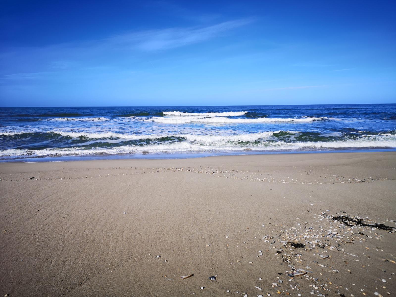 Strand mit Sand und Wellen, klarer Himmel und Meeresansicht.