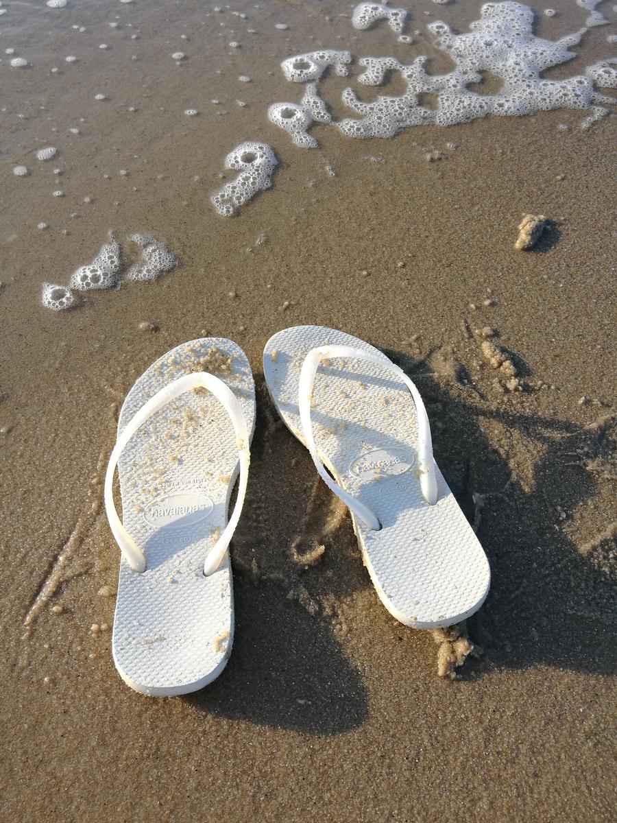 Weiße Flip-Flops liegen auf sandigem Strand mit Seifenblasen.