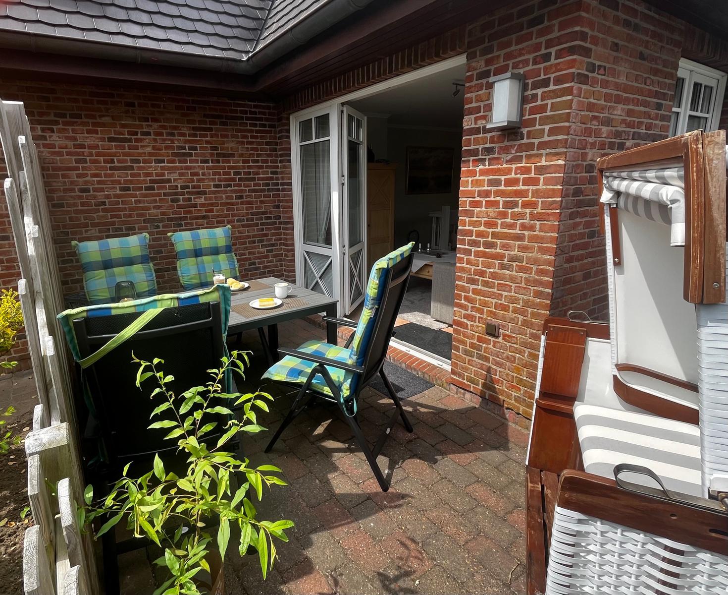 Terrasse mit Tisch, Stühlen und Strandkorb. Durchgang zur Wohnung.