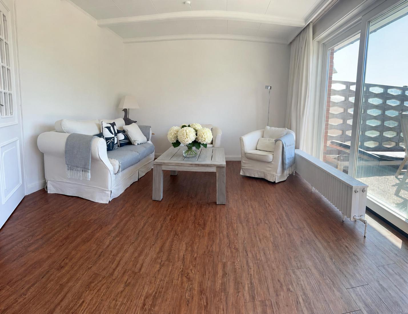 Wohnzimmer mit Sofa, Sessel und Tisch. Holzboden und großes Fenster.