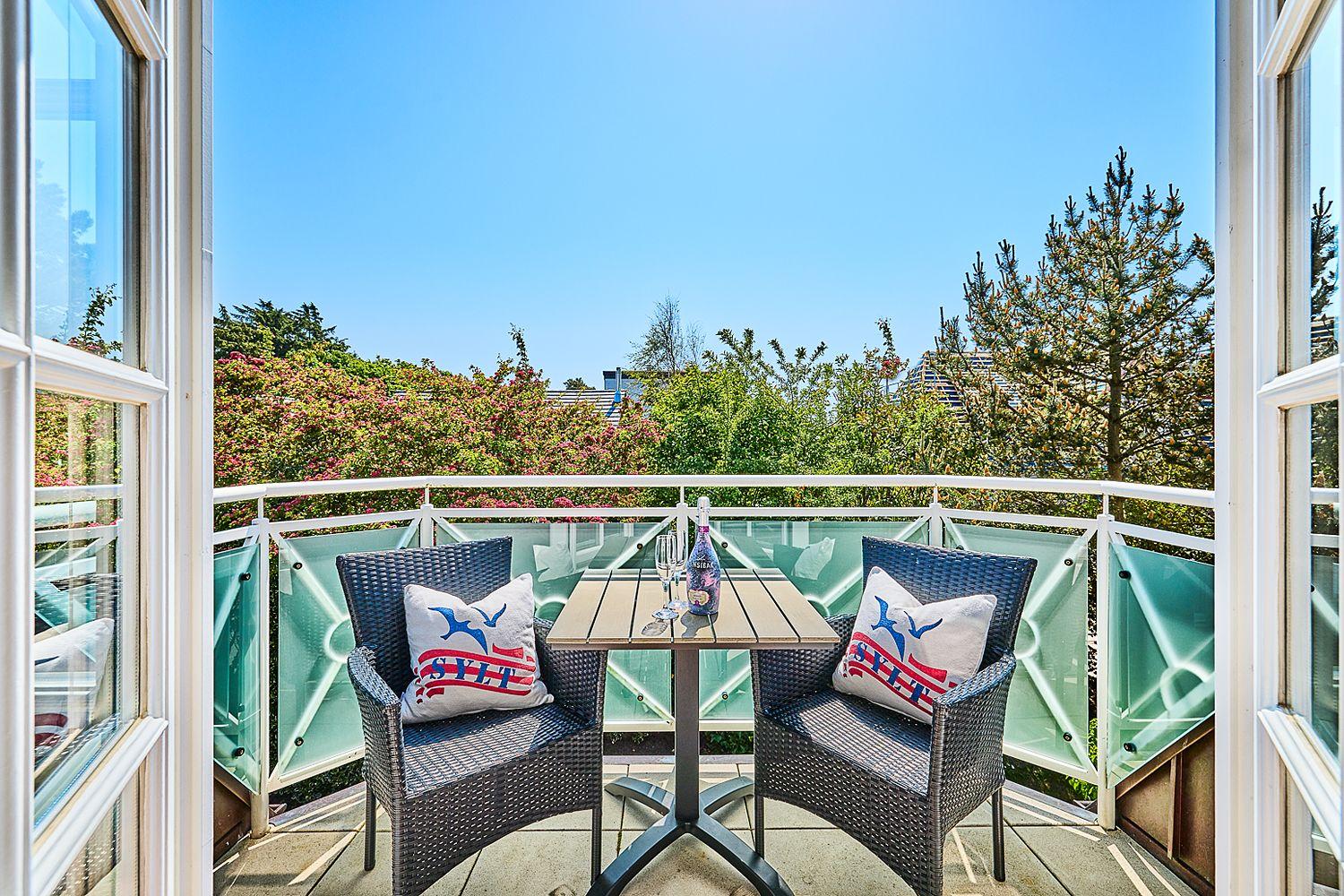 Balcony with two chairs, table, and view of greenery and sky.