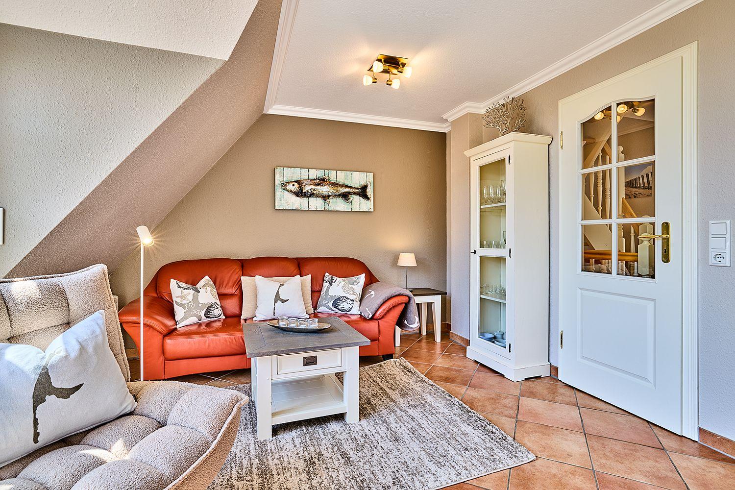 Wohnzimmer mit rotem Sofa, weißen Kissen und Holztisch. Tür führt zur Treppe.