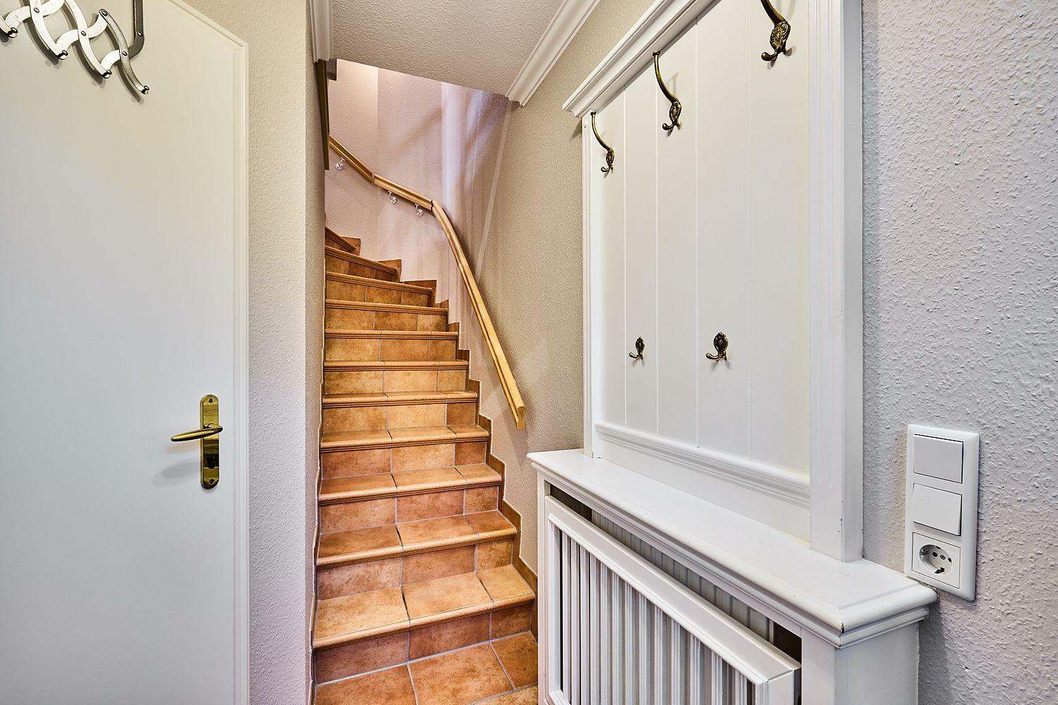 Hausflur mit Treppe, Garderobe und Heizkörper.