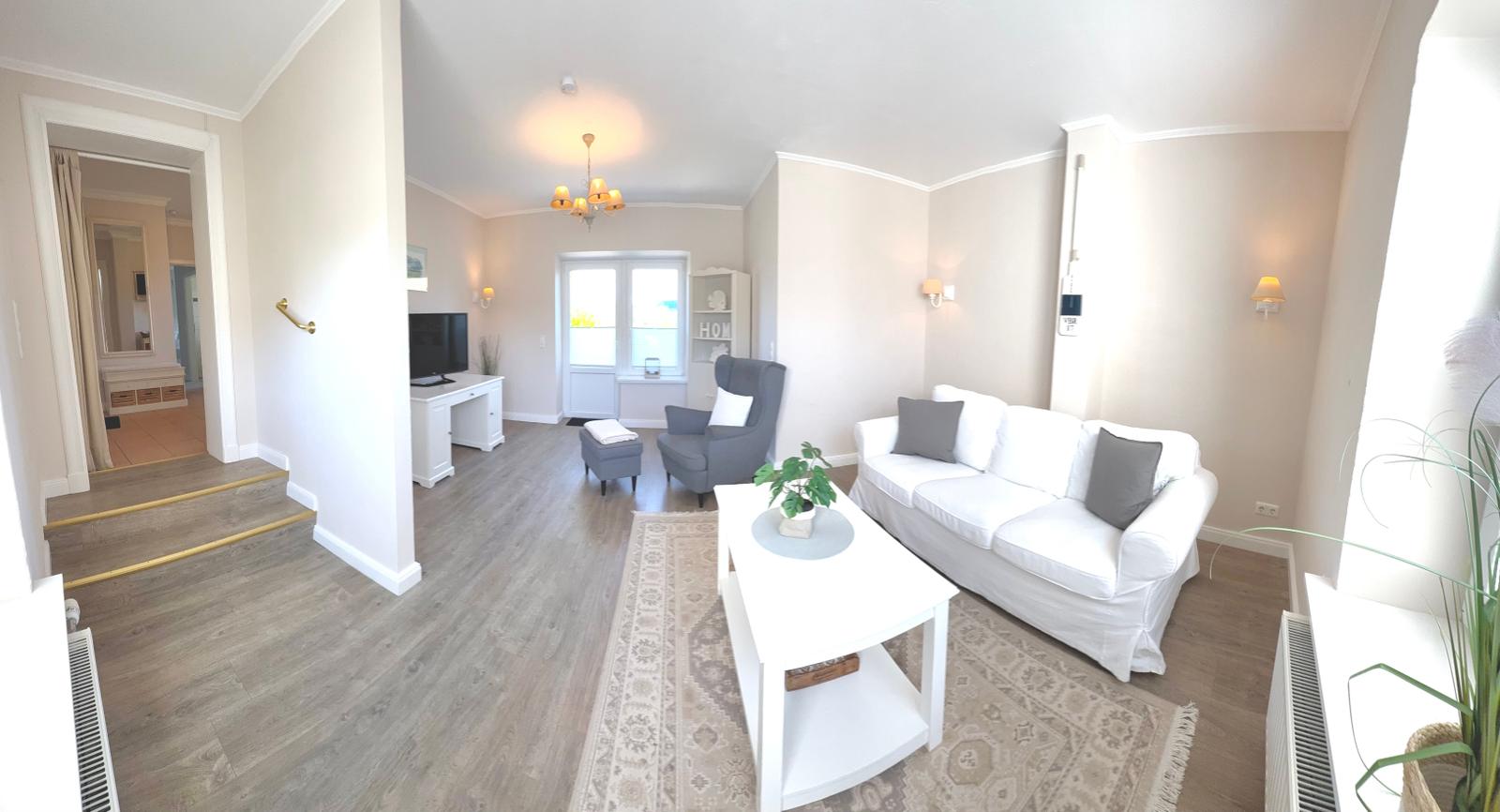 Wohnzimmer mit Sofa, Sessel und Fernseher. Holzfußboden und Teppich.