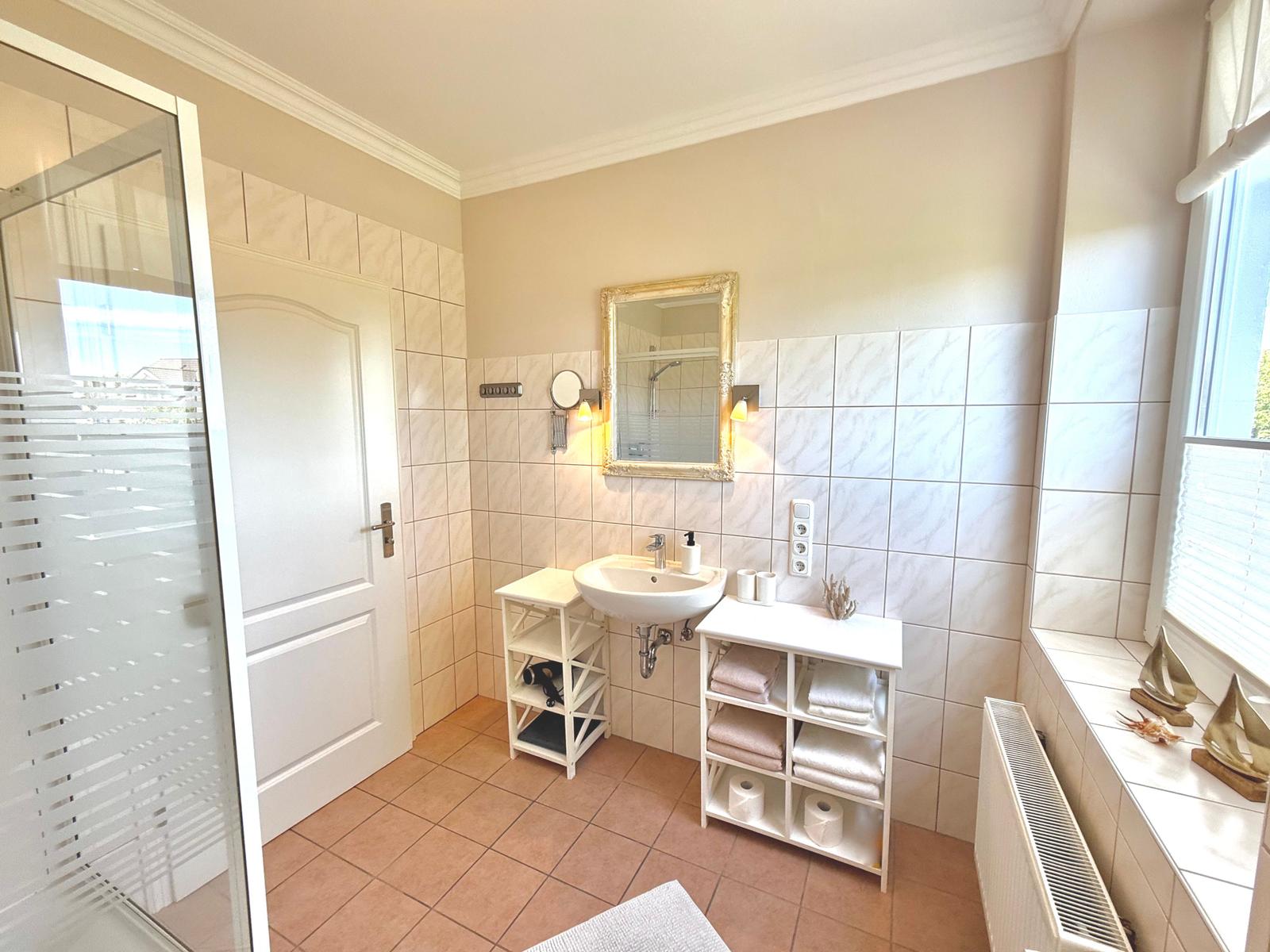 Badezimmer mit Dusche, Waschbecken und Fenster. Fliesenwand und Handtücher.
