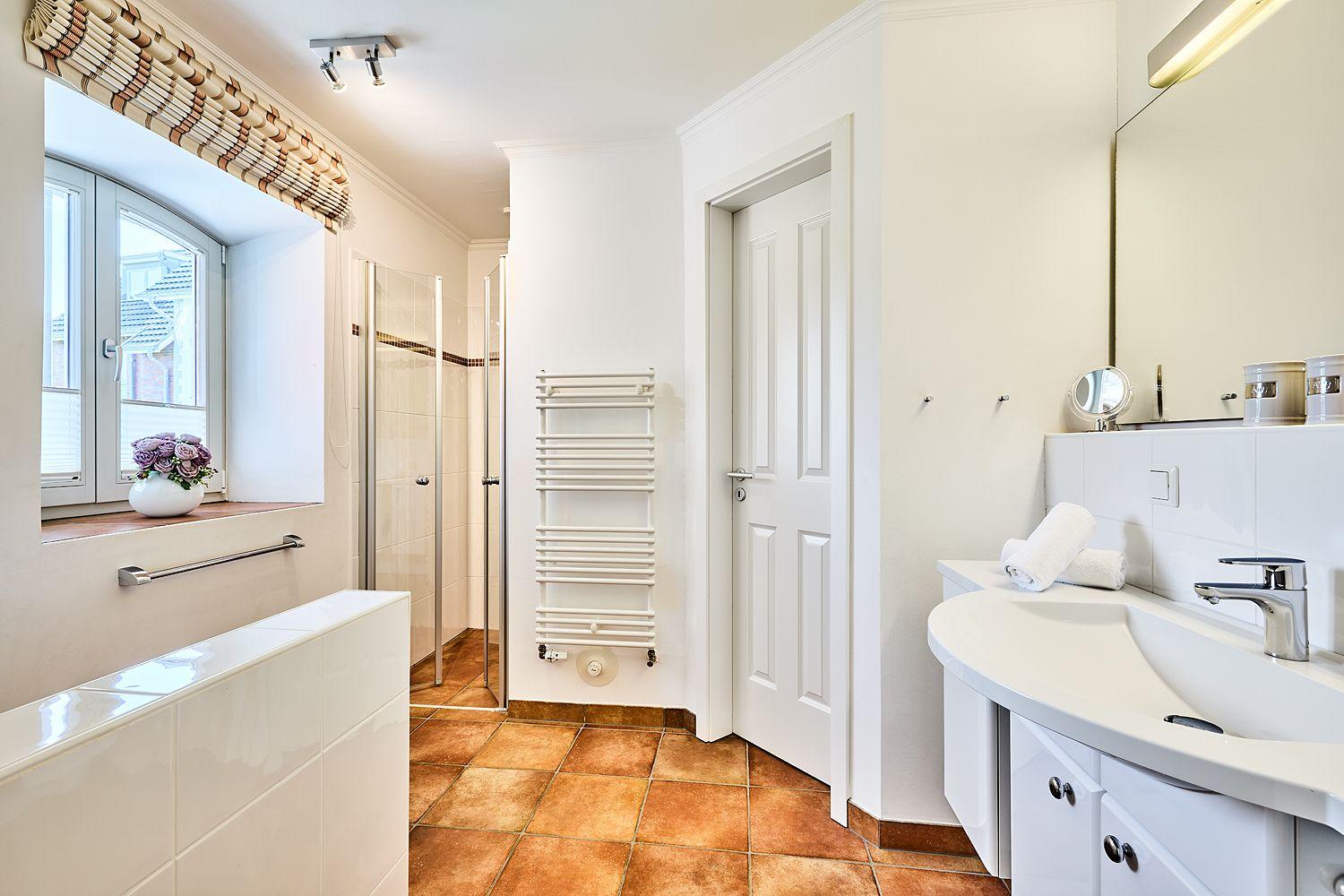 Badezimmer mit Dusche, Waschbecken und Fenster mit Blumen.