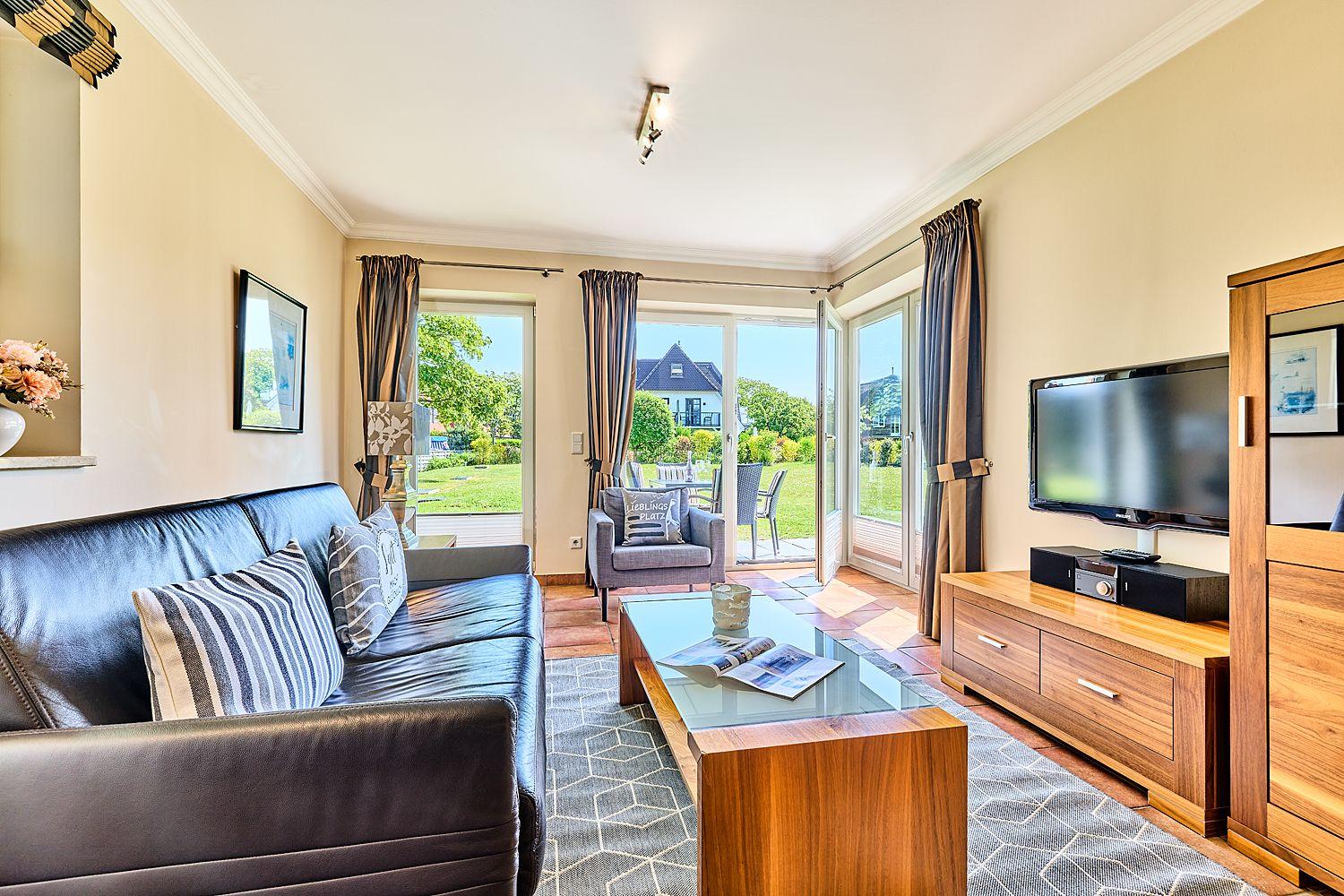 Wohnzimmer mit Sofa, Couchtisch und TV. Durchgang zur Terrasse mit Gartenansicht.