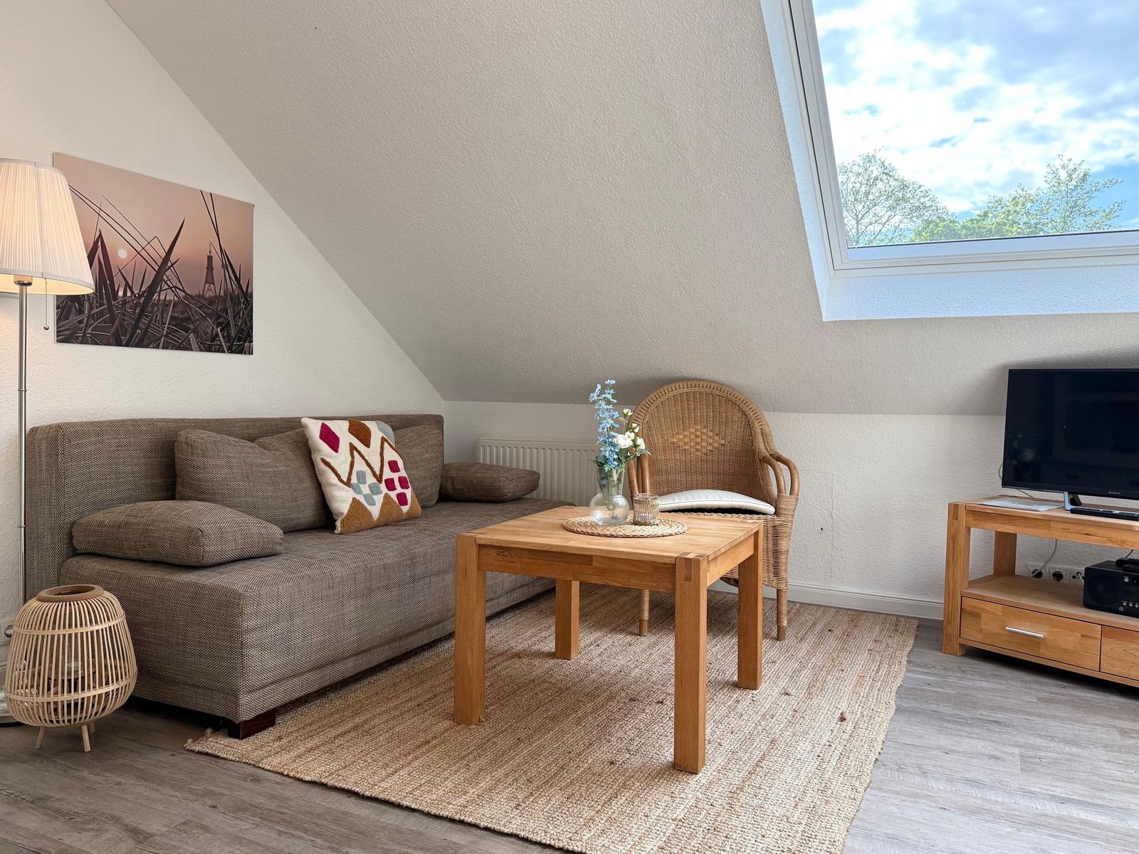 Wohnzimmer mit Sofa, Tisch, Stuhl und TV unter Dachschrägen mit Dachfenster.