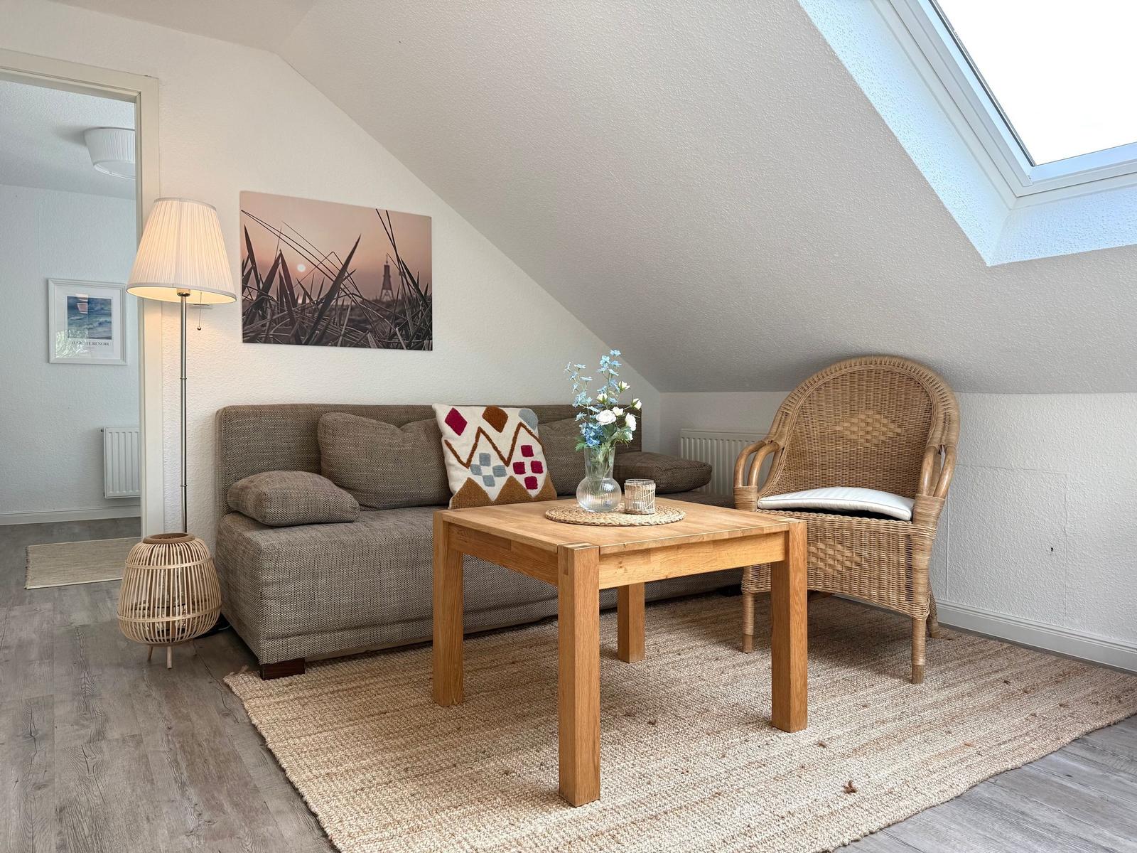 Wohnbereich mit Sofa, Rattan-Stuhl und Holztisch unter Dachschrägen.