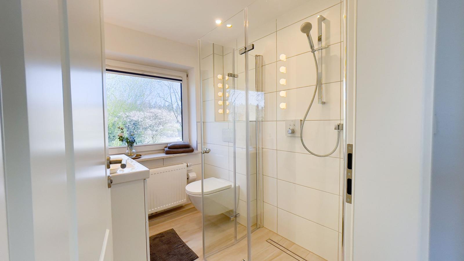 Badezimmer mit Dusche, Toilette und Fenster mit Blick auf Garten.