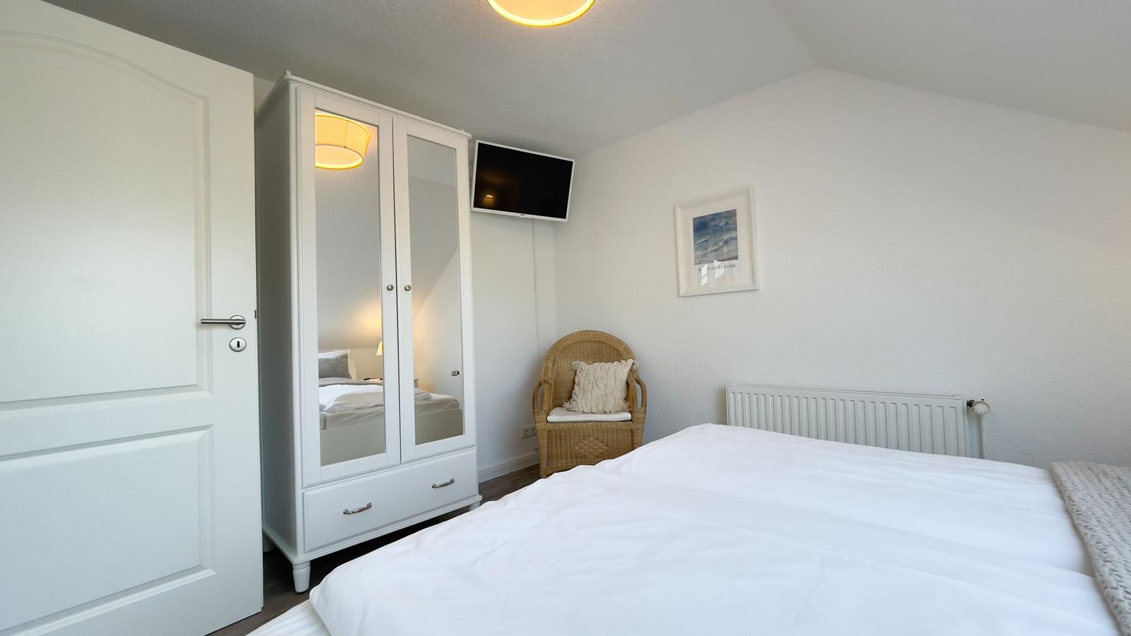 Schlafzimmer mit Bett, Kleiderschrank, Sessel und Wandbild.