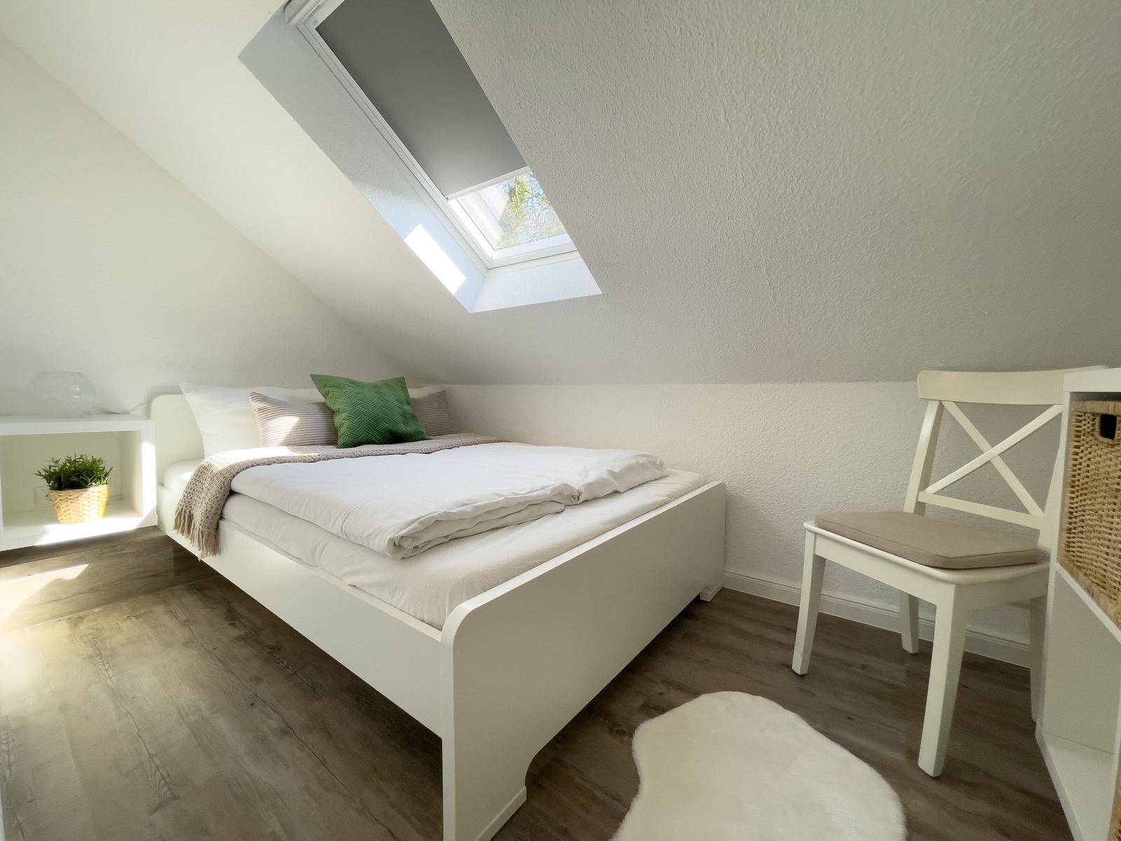 Ein Schlafzimmer mit Dachfenster, weißem Bett und Stuhl.