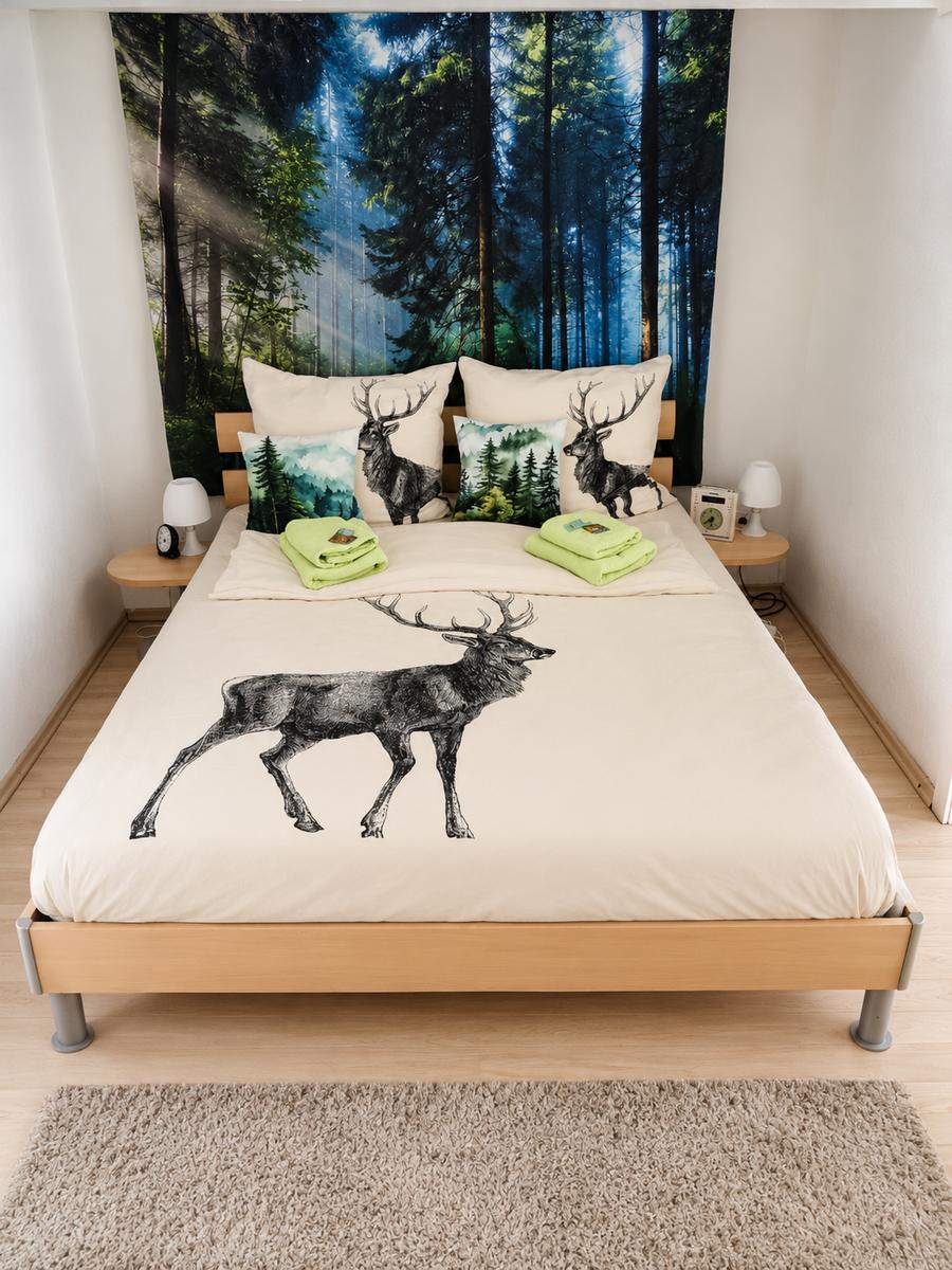 Schlafzimmer mit Bett, Wandbild Wald und Kissen mit Hirschmotiv.