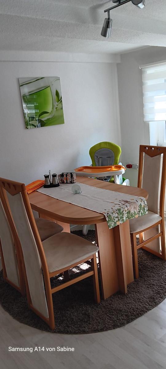 Esstisch mit vier Stühlen und Hochstuhl. Wandbild und Fenster mit Jalousie.