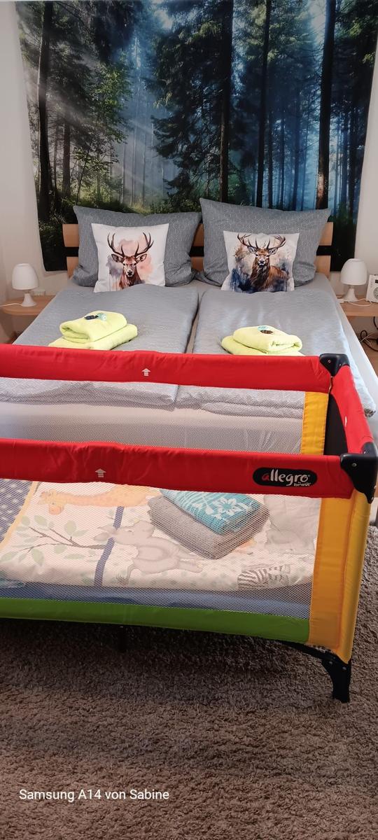 Zimmer mit Doppelbett, Babybett und Waldtapete an der Wand.