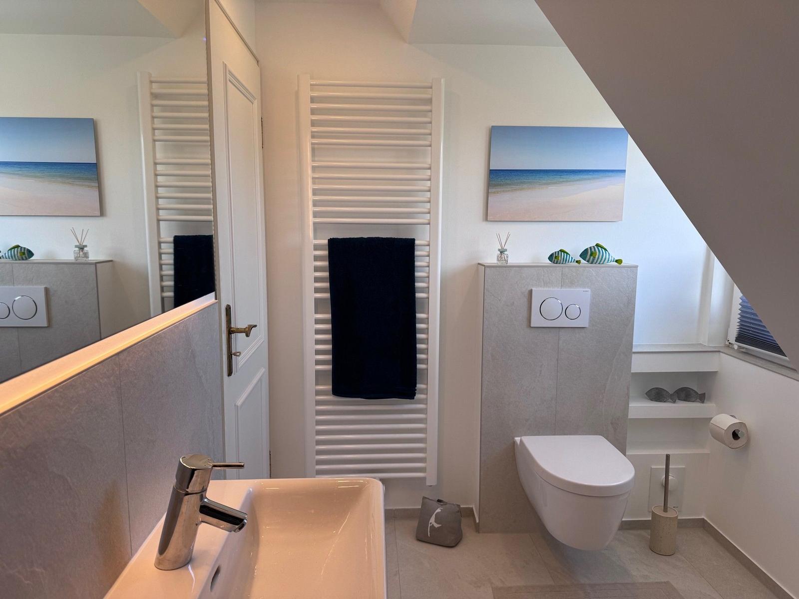 Badezimmer mit Waschbecken, Toilette und Handtuchhalter unter Dachschrägen.