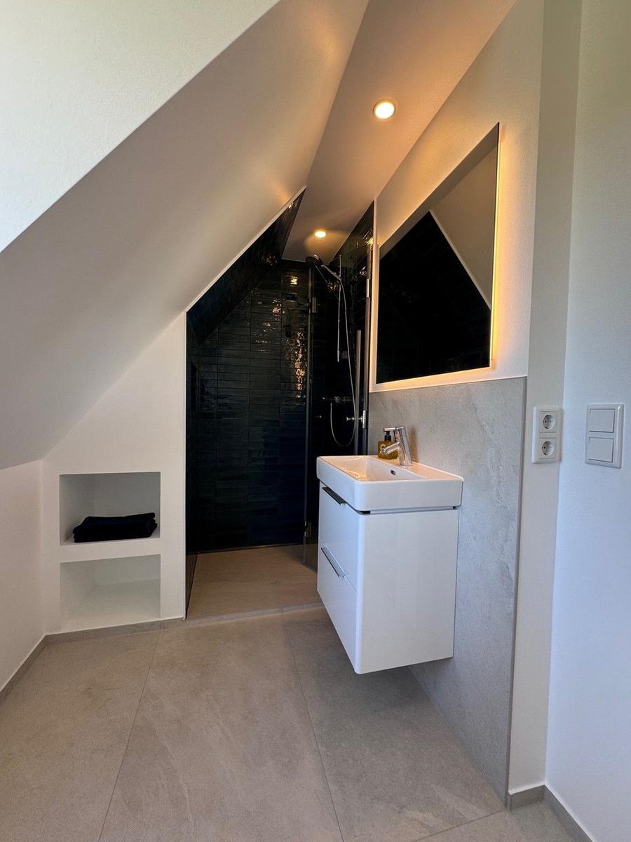 Dusche mit Glaswand, Waschbecken und Spiegel unter Dachschrägen.