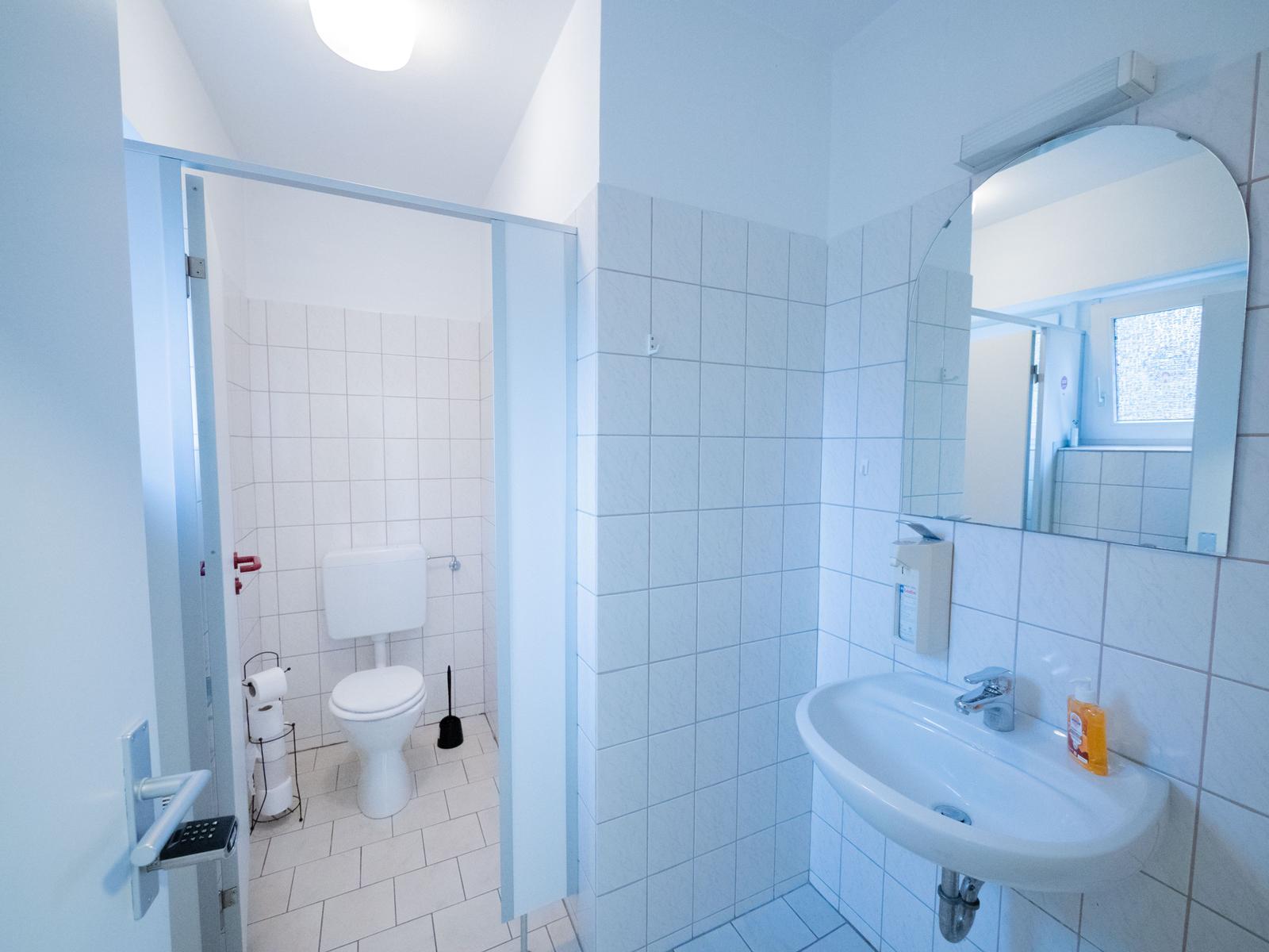 Badezimmer mit Waschbecken, Spiegel und Toilettenbereich hinter Glastür.