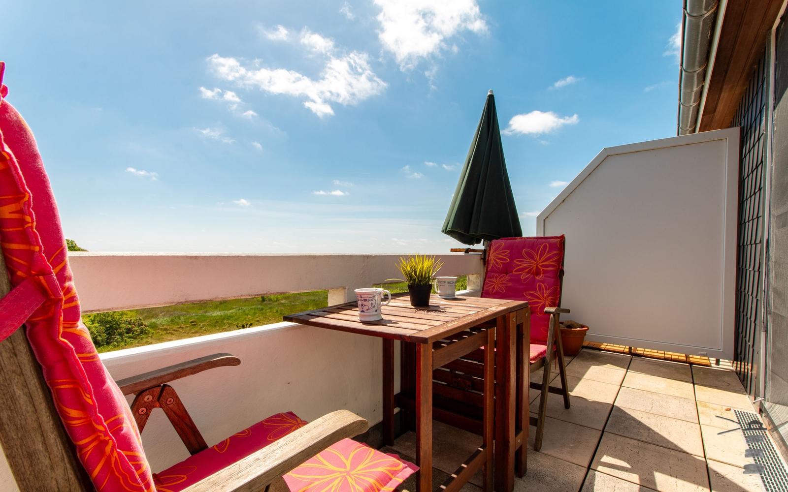 Terrasse mit Tisch, zwei Stühlen, Sonnenschirm und Blick auf Grünland.