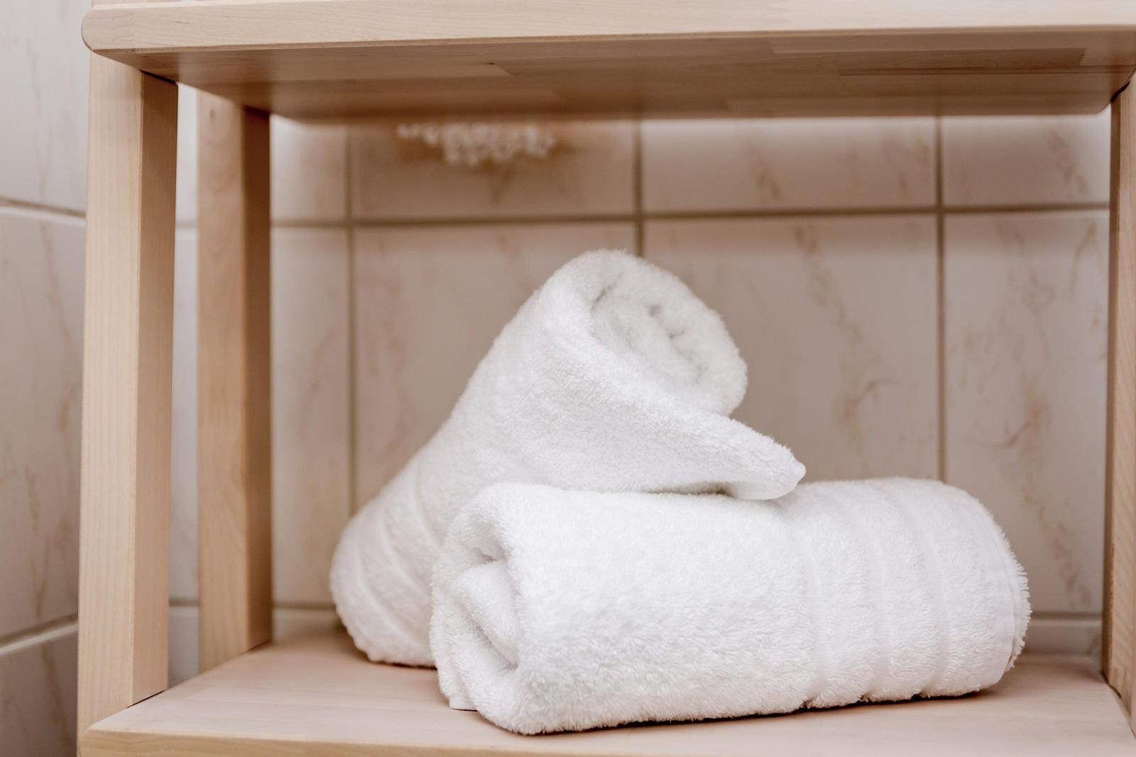 Zwei weiße Handtücher liegen auf einem Holzregal in einem Badezimmer.