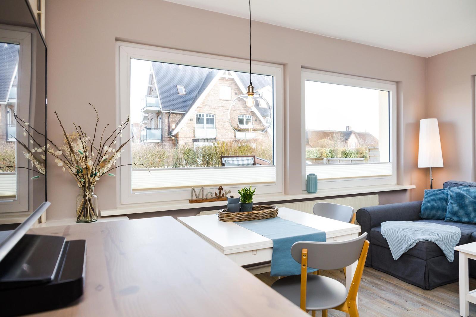 Wohn- und Essbereich mit Fenstern, Tisch, Stühlen und Sofa.