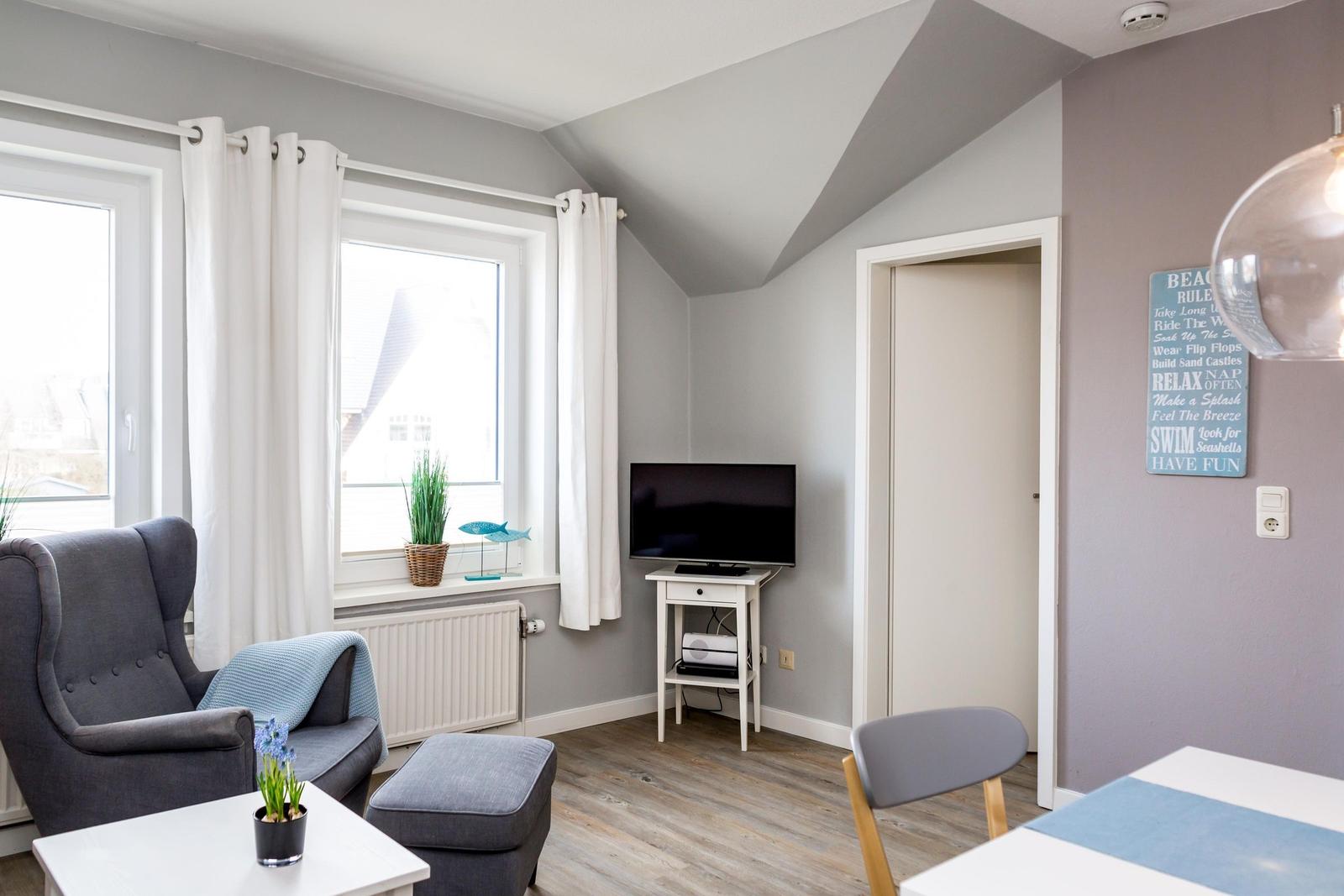 Wohnzimmer mit Sessel, Fernseher und Fenster. Wand mit Strandregeln.