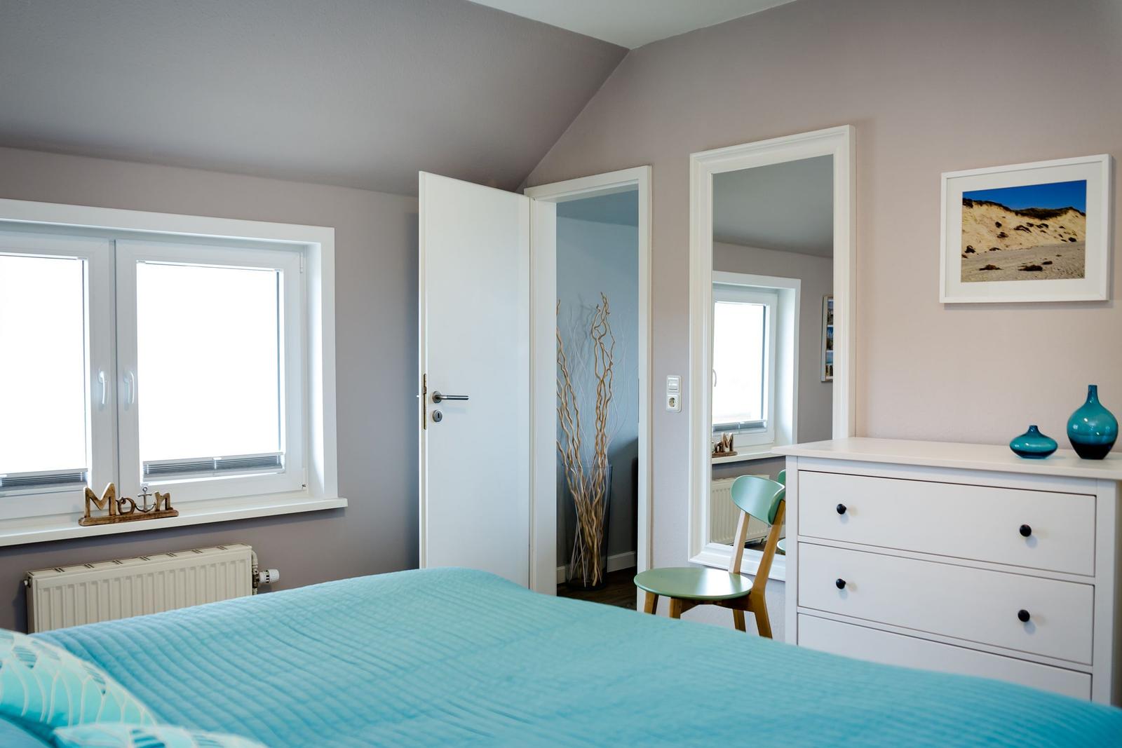 Schlafzimmer mit Bett, Schrank und Fenster. Tür führt in angrenzenden Raum.