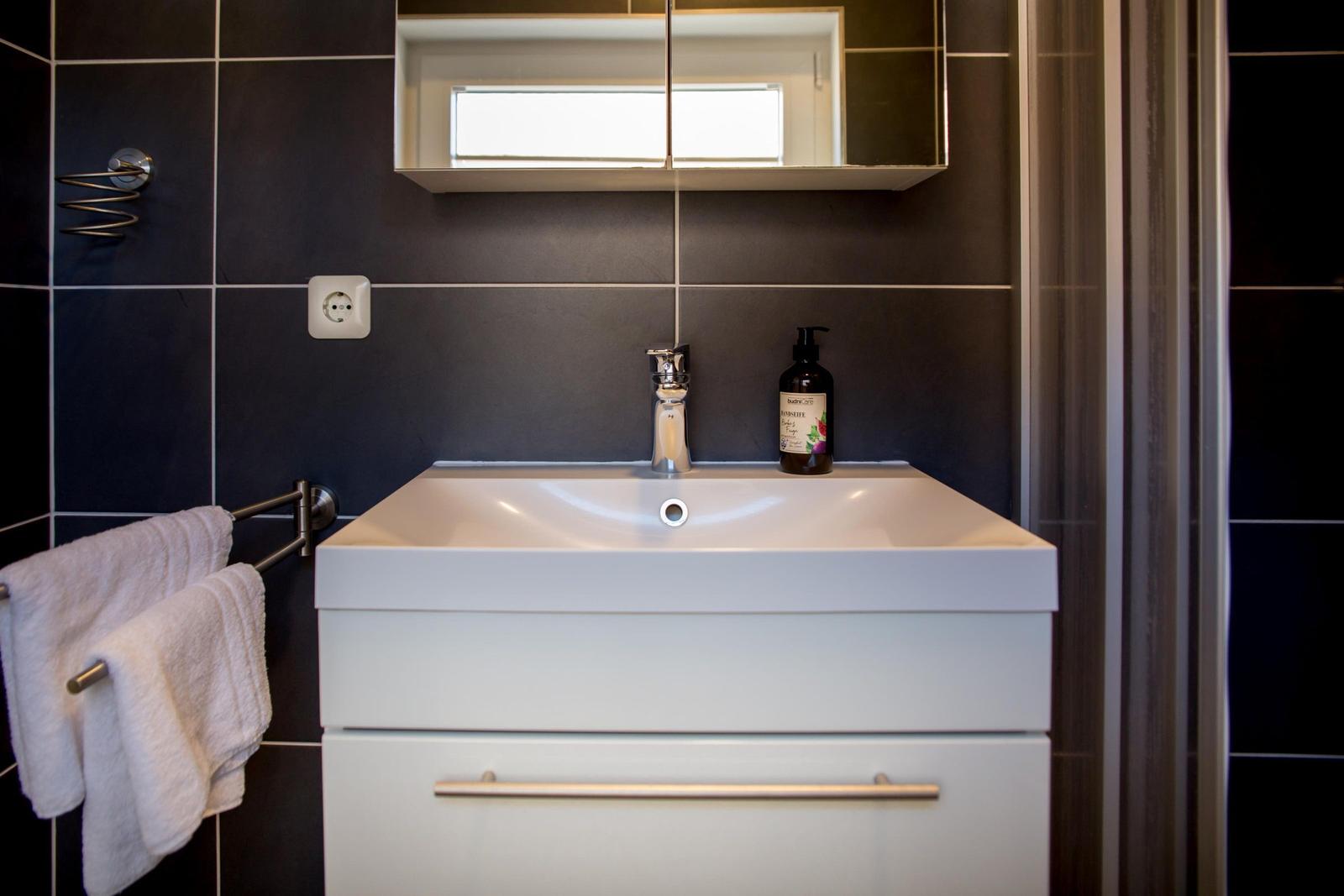 Badezimmer mit Waschbecken, Spiegel und Handtuchhalter an dunkler Wand