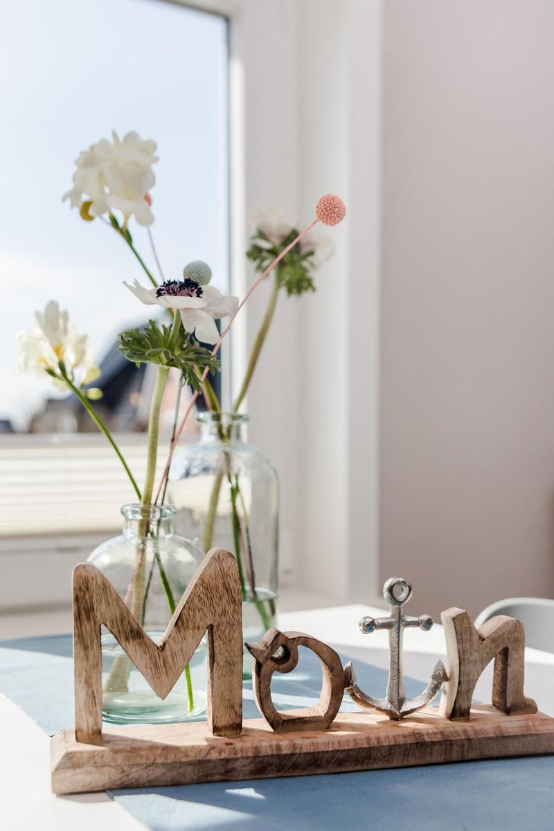 Holz-Schild mit Anker und Blumen in Glasflaschen auf Tisch