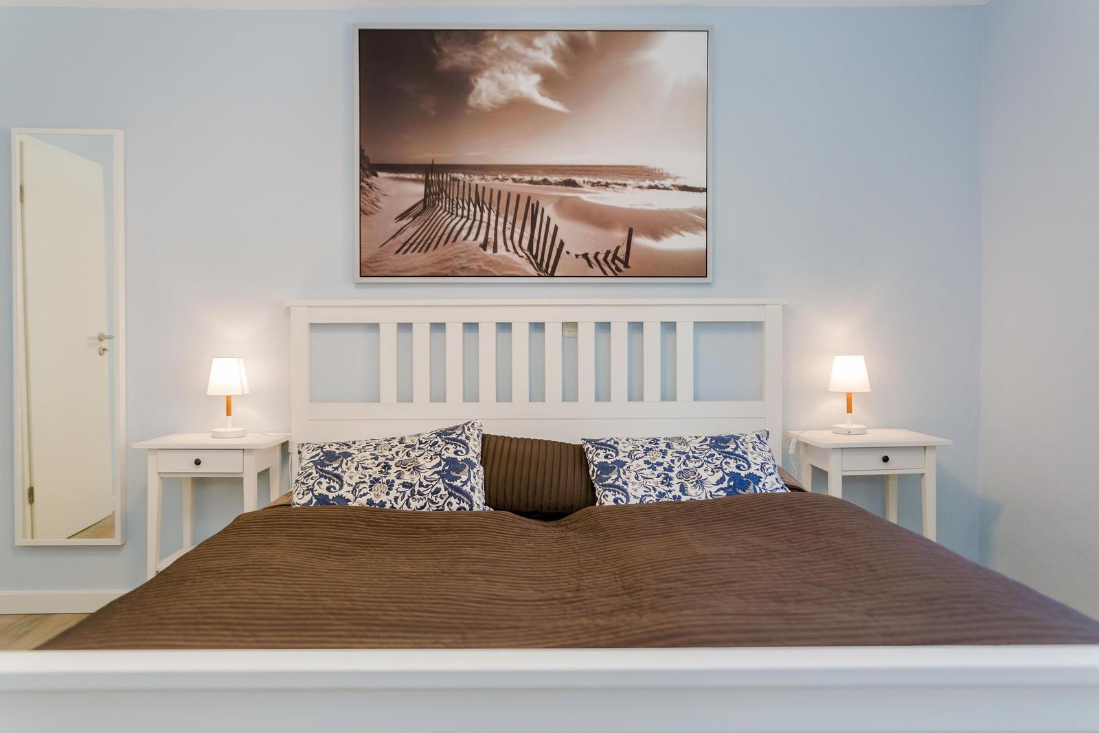 Schlafzimmer mit weißem Bett, zwei Nachttischen und Wandbild