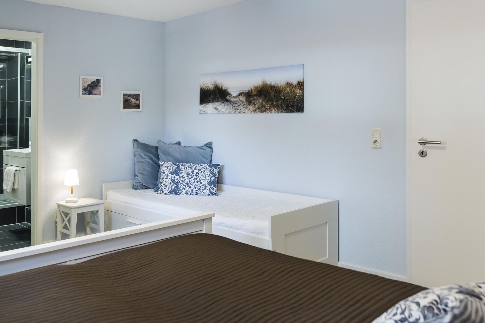 Schlafzimmer mit weißem Bett, blauen Wänden und Strandbildern an der Wand.