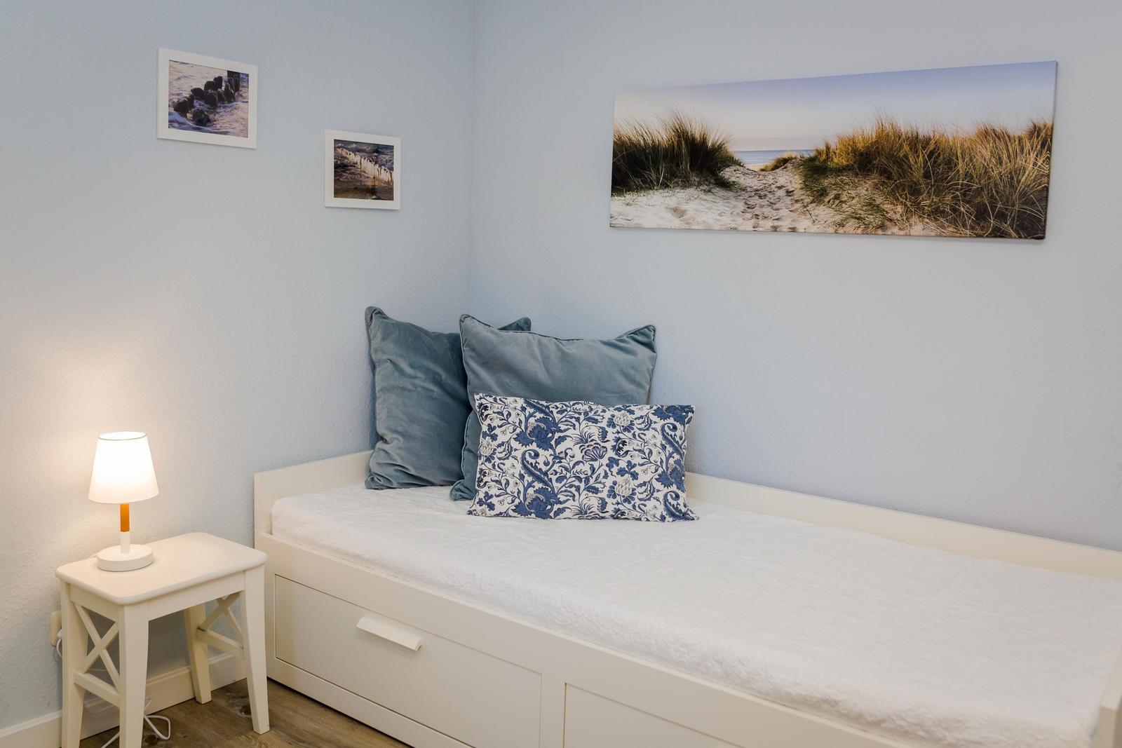 Ein Schlafzimmer mit weißem Bett, Kissen und Wandbildern an hellblauen Wänden.
