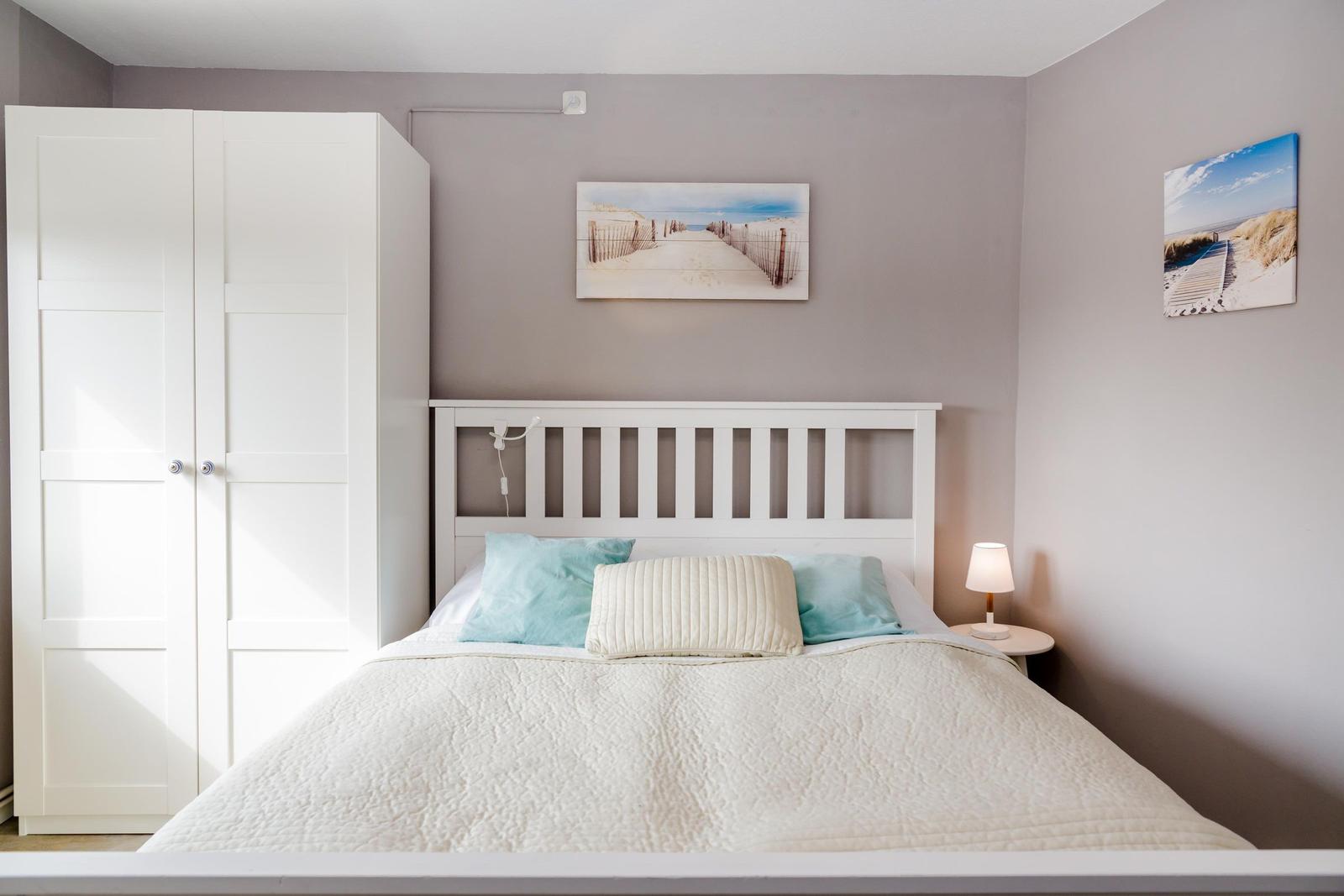 Schlafzimmer mit weißem Bett, Kleiderschrank und Wandbildern