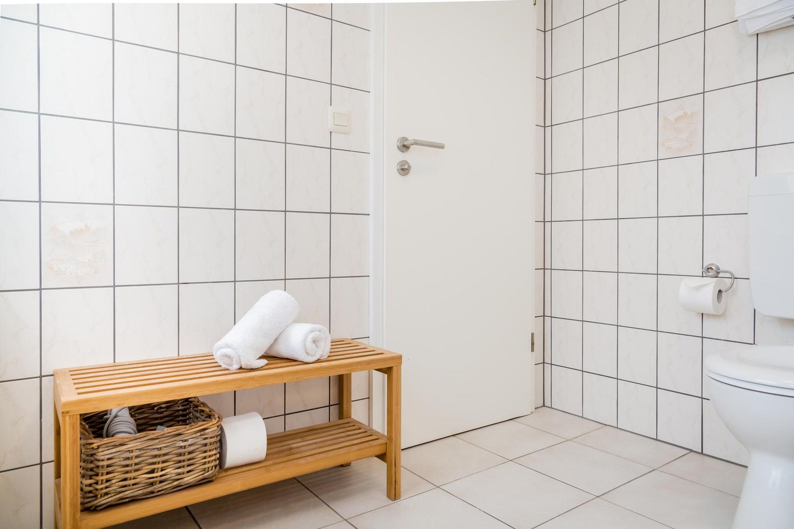 Badezimmer mit Toilette, Holzbank und gefalteten Handtüchern.