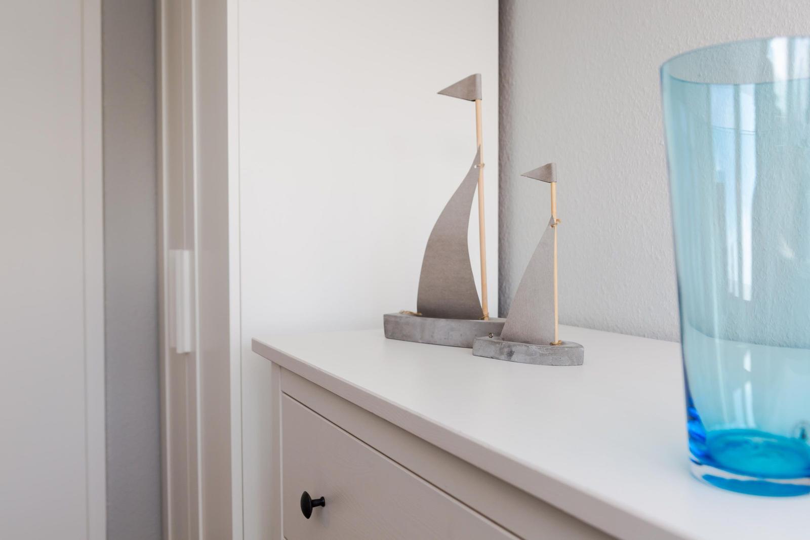 Two sailboats and a blue glass vase on a white dresser.
