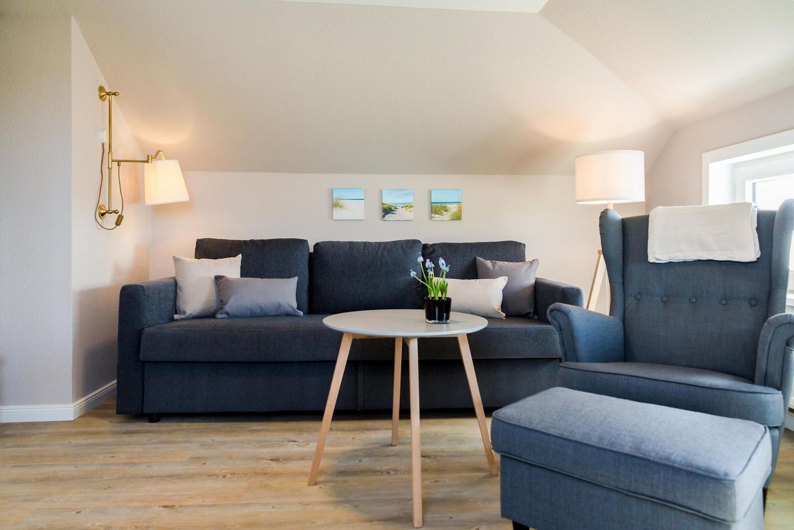 Living room with sofa, armchair, and table. Wall art and floor lamp visible.