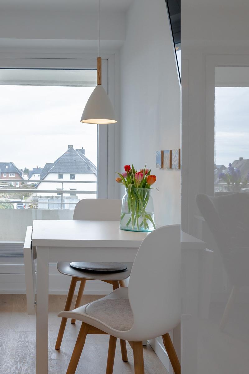 Essbereich mit weißem Tisch, Stühlen und Blumen in Glas. Fenster mit Blick auf Wohngebiet.