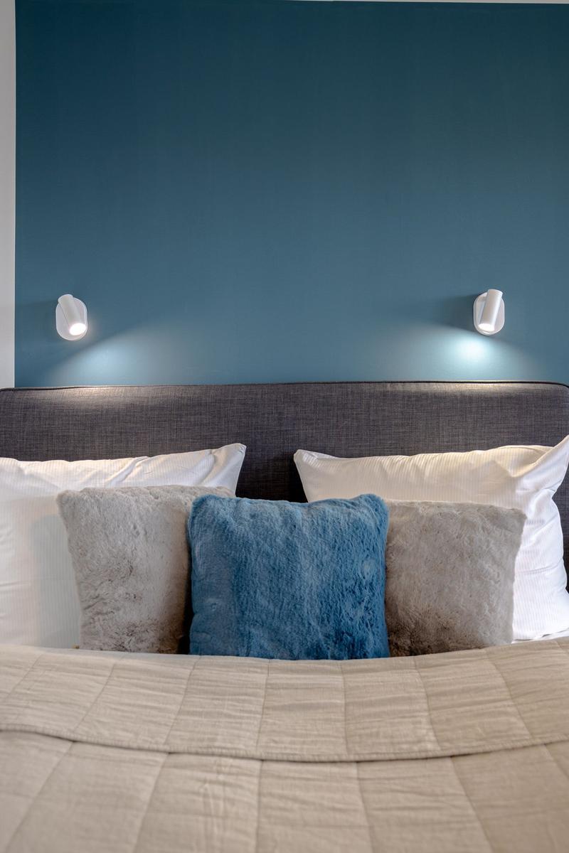 Doppelbett mit Kissen und blauer Wand mit Wandlampen.