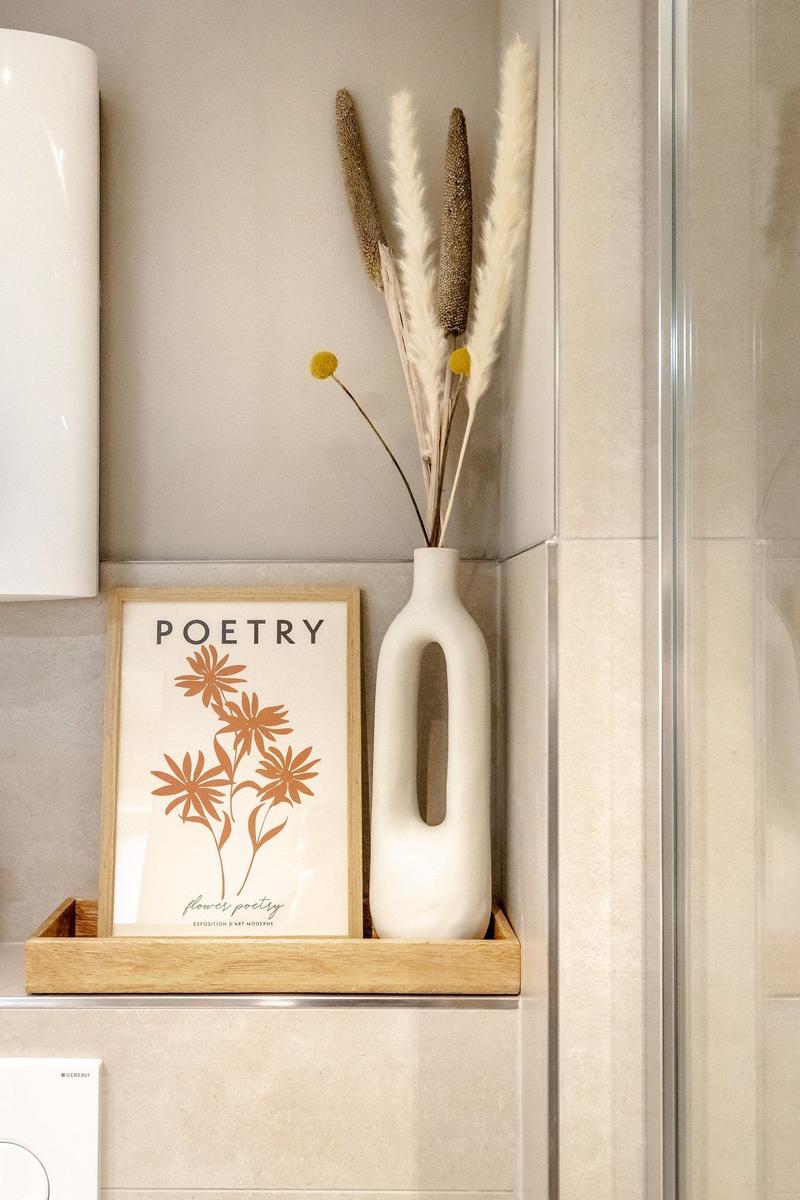 Badezimmer-Ecke mit Vase, Trockenblumen und Bild mit Blumenmotiv.