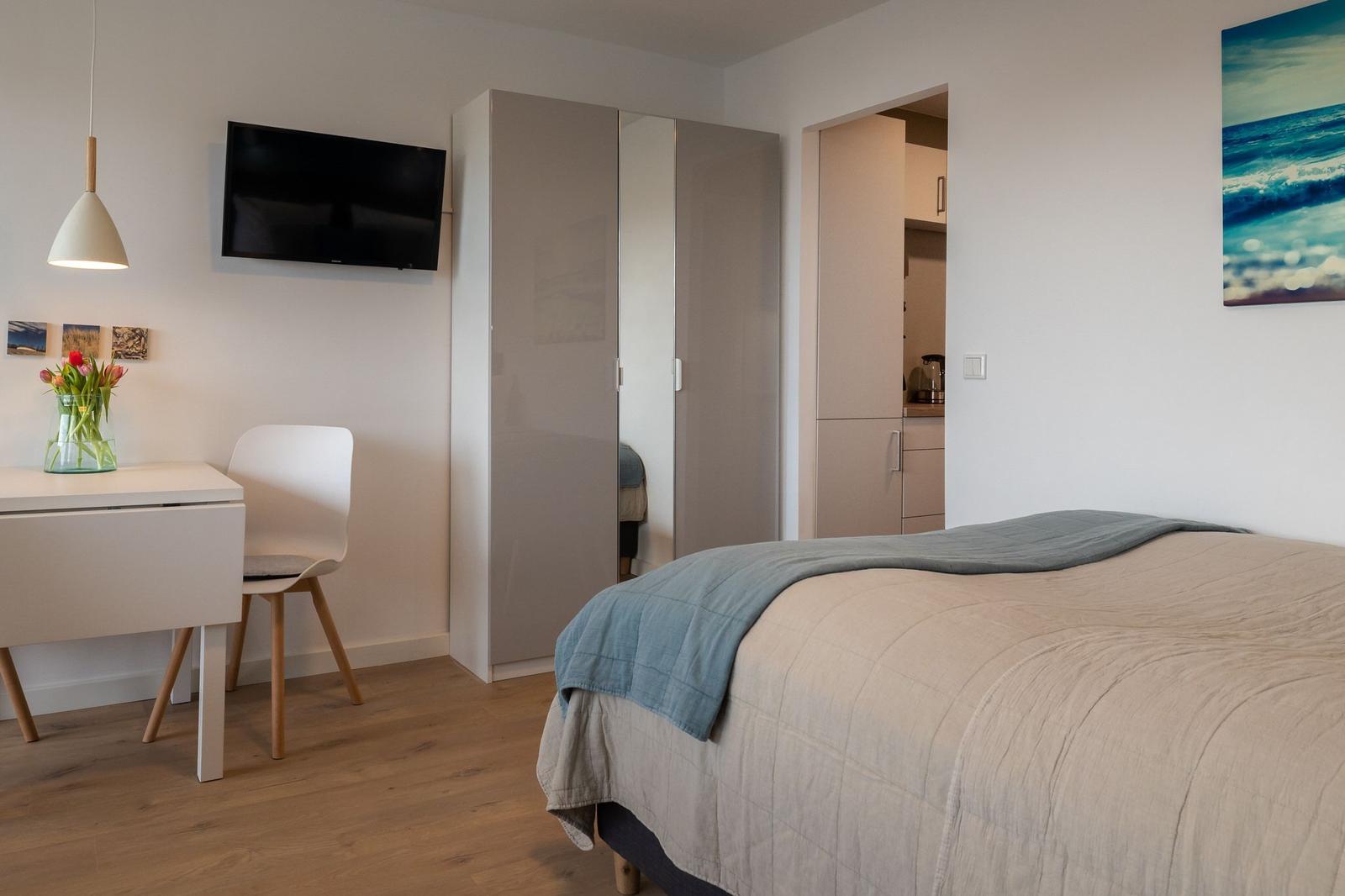 Schlafzimmer mit Bett, Schreibtisch, Kleiderschrank und Fernseher.